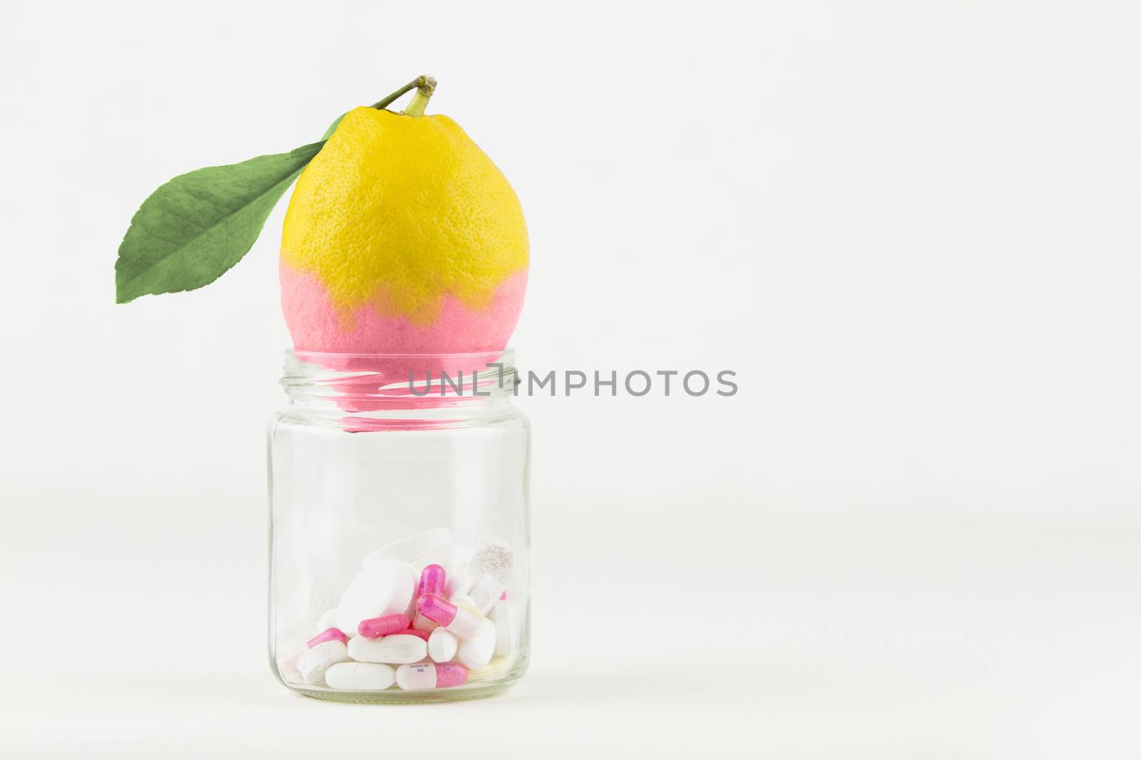 Concept: manipulation of human GMO of nature and related poisoned fruits. Close-up of a glass jar with a contaminated lemon changing color from the medicines in the jar on a white background