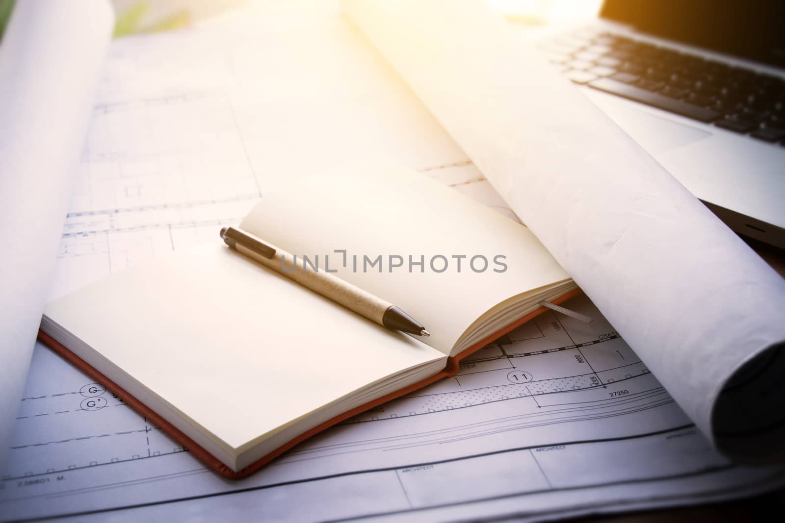 architect workplace background : notebook on blueprints for architectural plan with laptop on table in architect man working office, Vintage light effect.