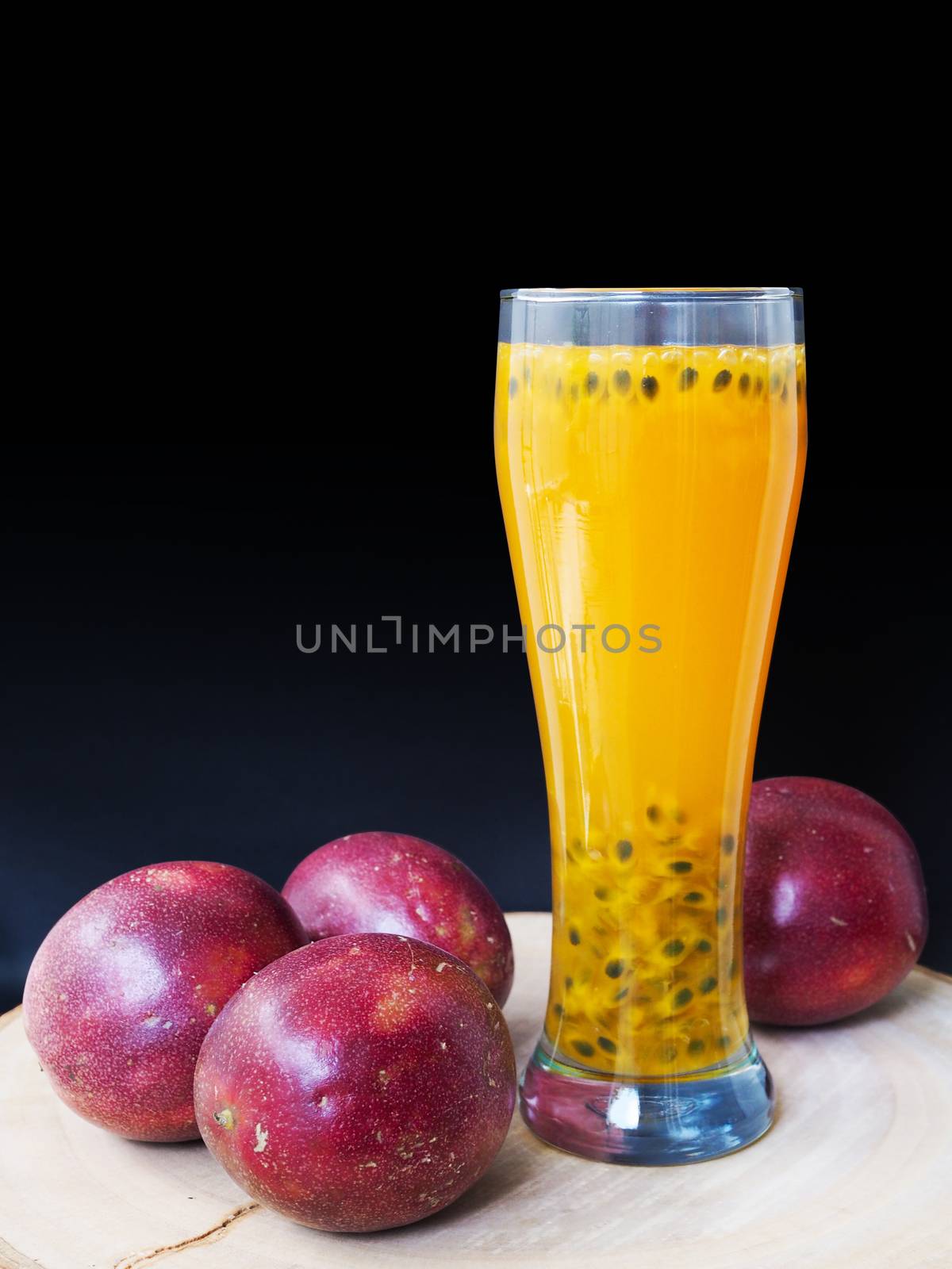 Refreshing drink with yellow juice in a glass made from passion fruit, bright red color on black background.