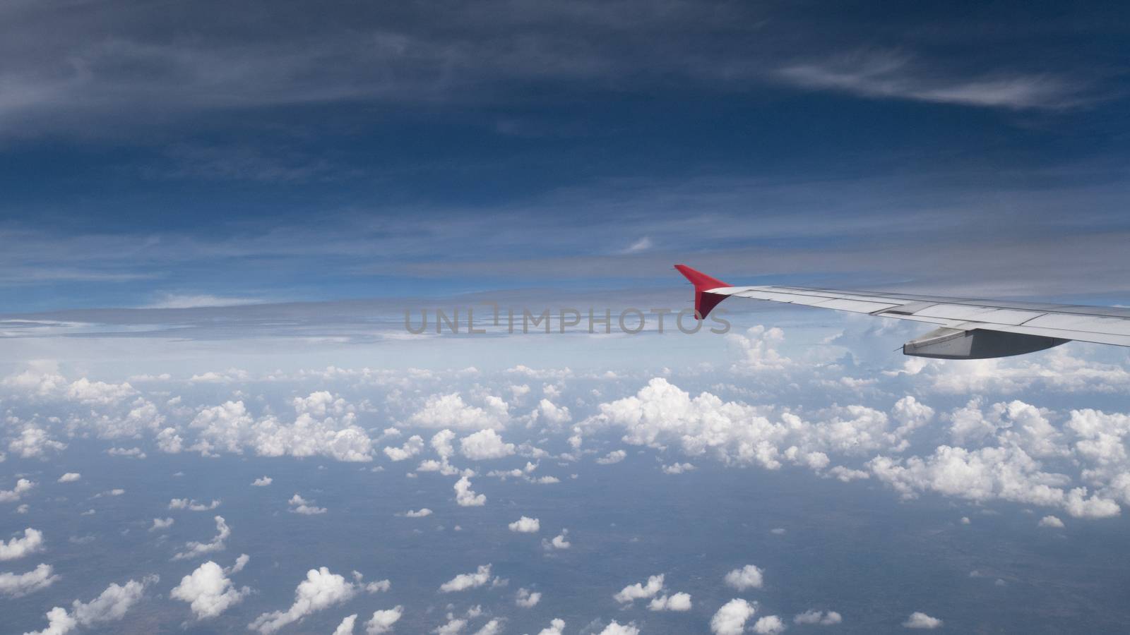 Plane travel concept : View from aircraft window. Clouds and blue sky under airplane wing as seen through window of an airplane in wide angel with copy space for travel agency background