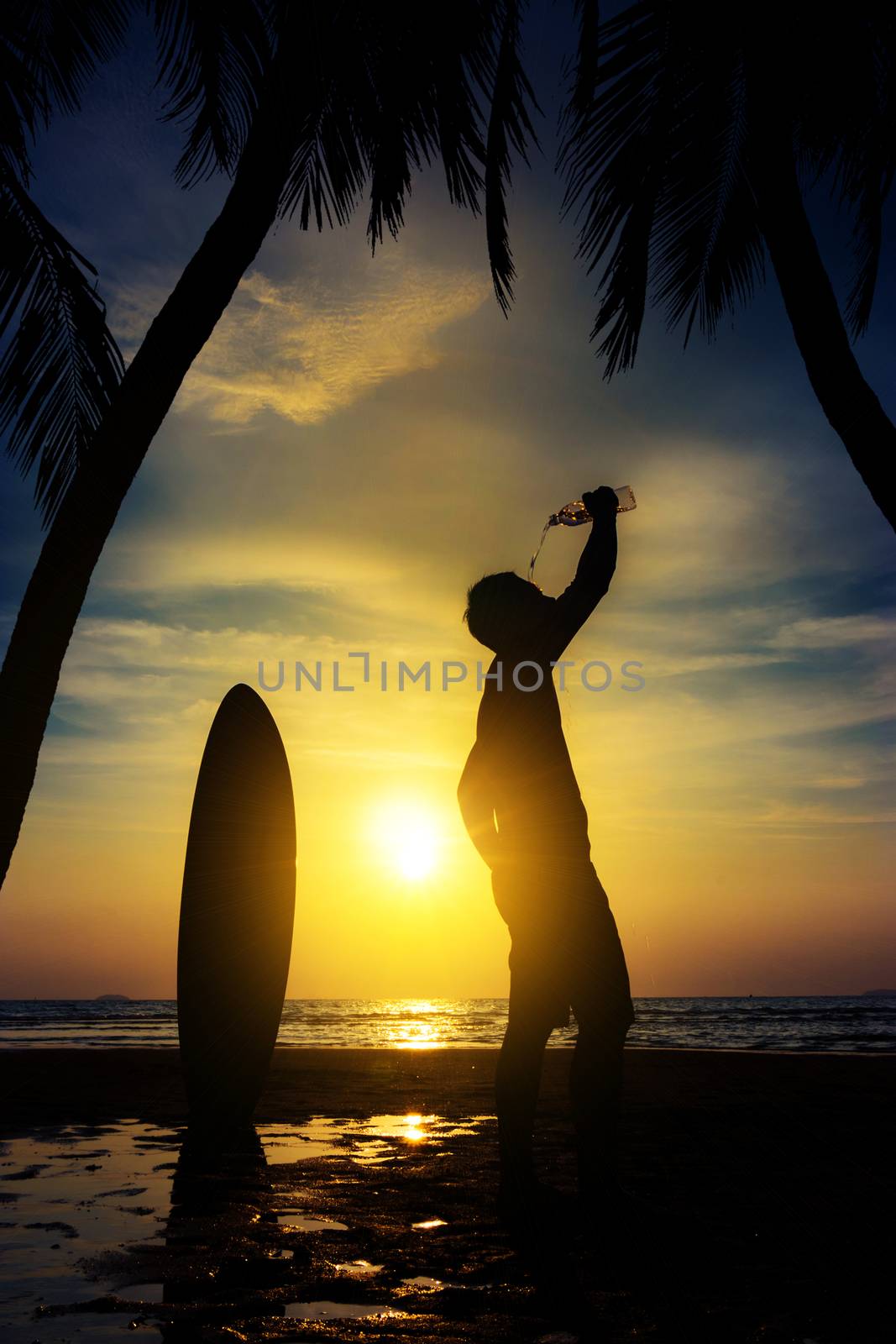 Silhouette of surf man stand with a surfboard and coconut palm drink water from bottle. Surfing at sunset beach. Outdoor water sport adventure lifestyle.Summer activity. Asia male model in his 20s by asiandelight