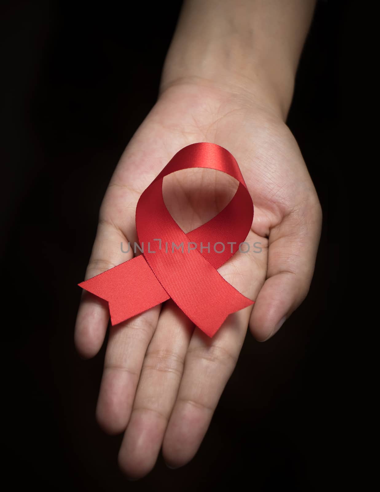 Red ribbon awareness on woman human hand : World aids day satin ribbon symbolic concept raising concerns/ help campaign on people health public support on HIV STD heart disease by asiandelight