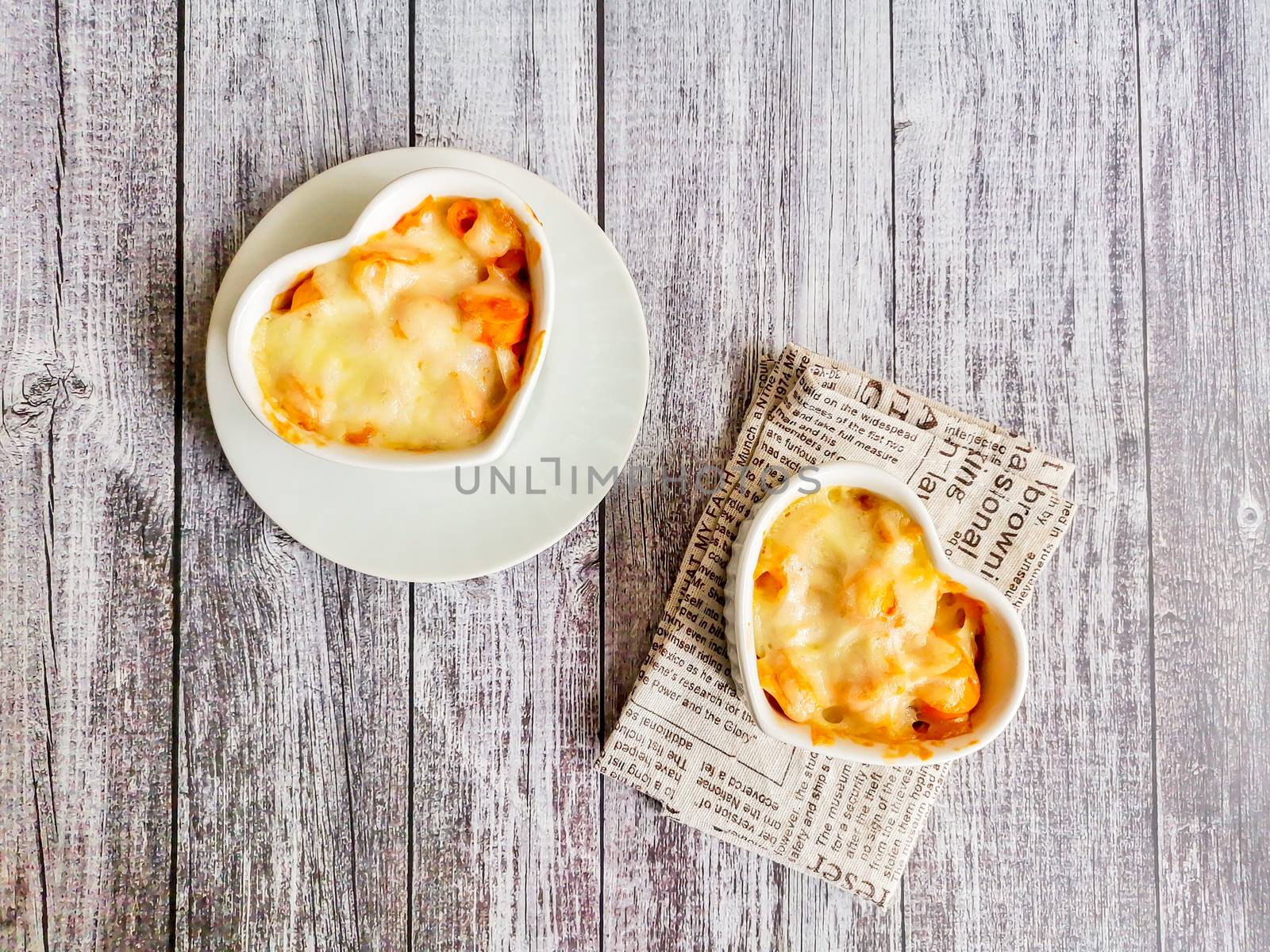 Top view macaroni and cheese in white heart shape bowl on wooden table with copyspace. Homemade food for lunch. 