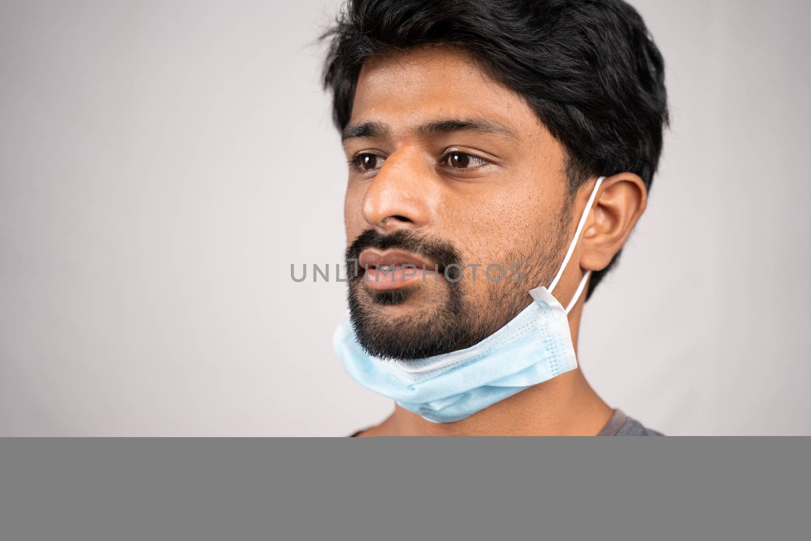 concept showing of improper way of using face masks during coronavirus or covid-19 crisis - young man wearing medical at neck on isolated background.