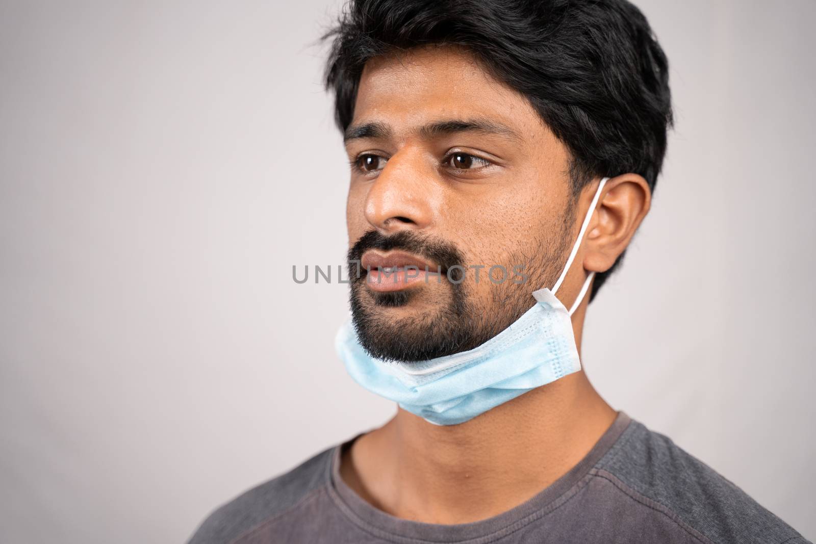 concept showing of improper way of using face masks during coronavirus or covid-19 crisis - young man wearing medical at neck on isolated background.