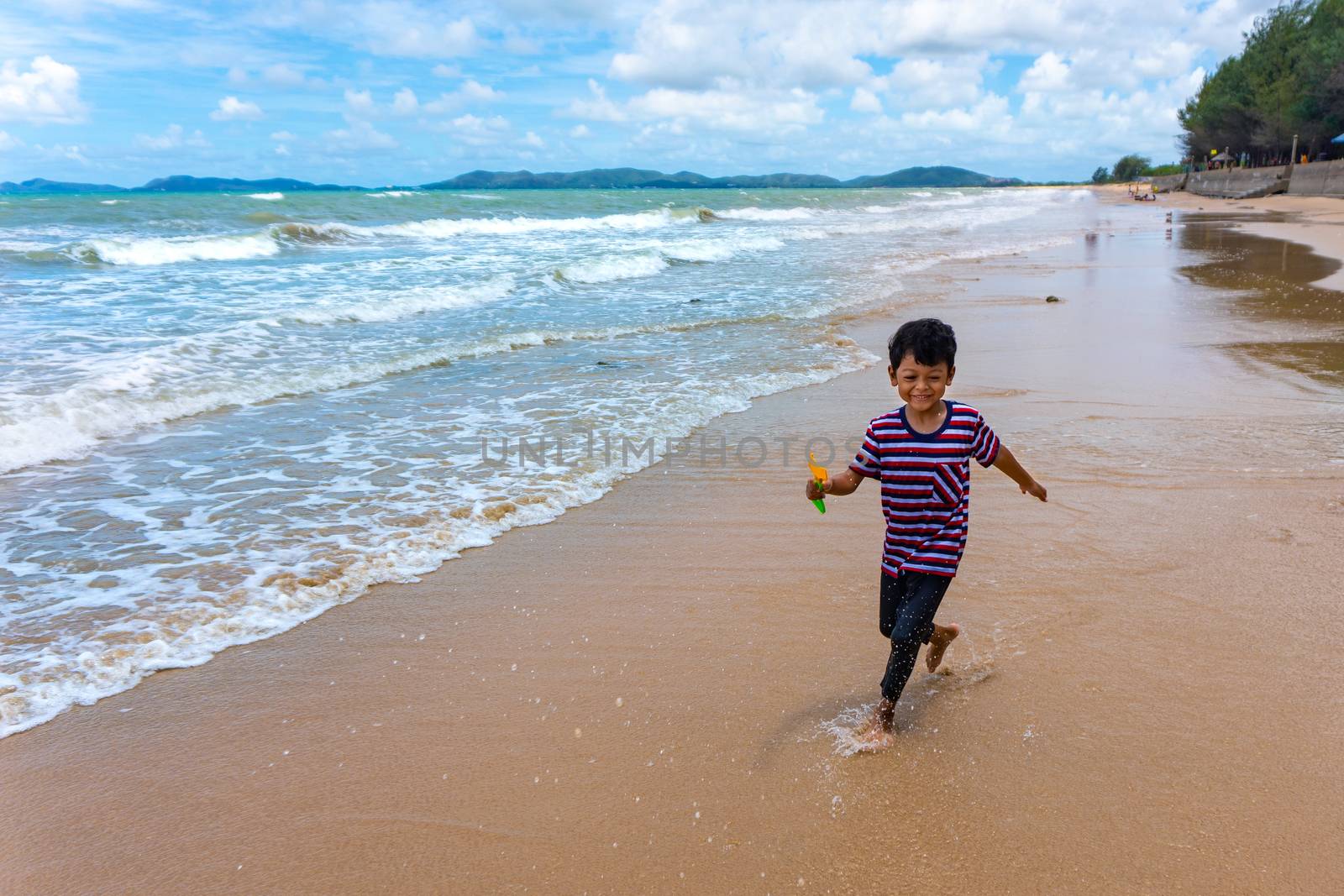 Asian kid play running in the sea and enjoying life during the summer holidays on the Phala Beach, Ban Chang District, Rayong, Thailand.