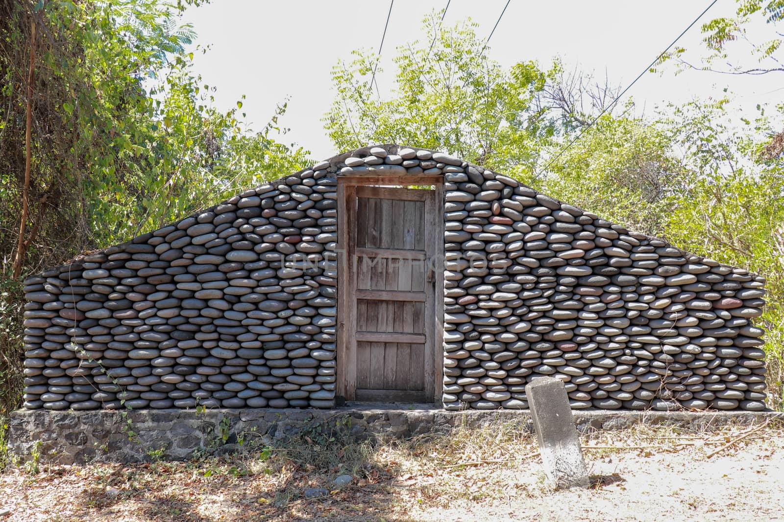 Stone wall with closed old wooden door by the road. A wall of pebbles in the jungle. Stones from the river that the water worked into smooth.