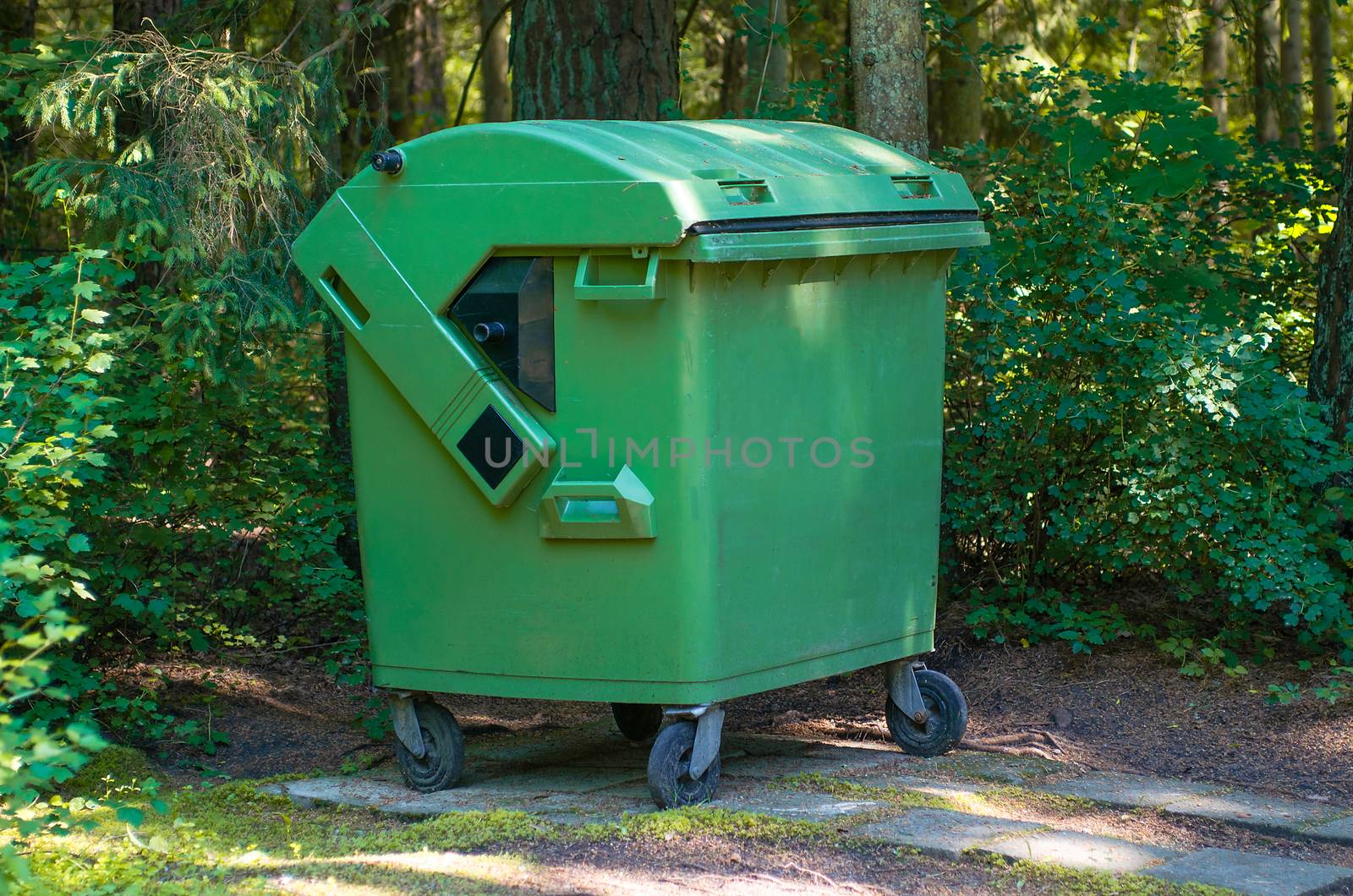 Green container with household waste against the green wood by KajaNi