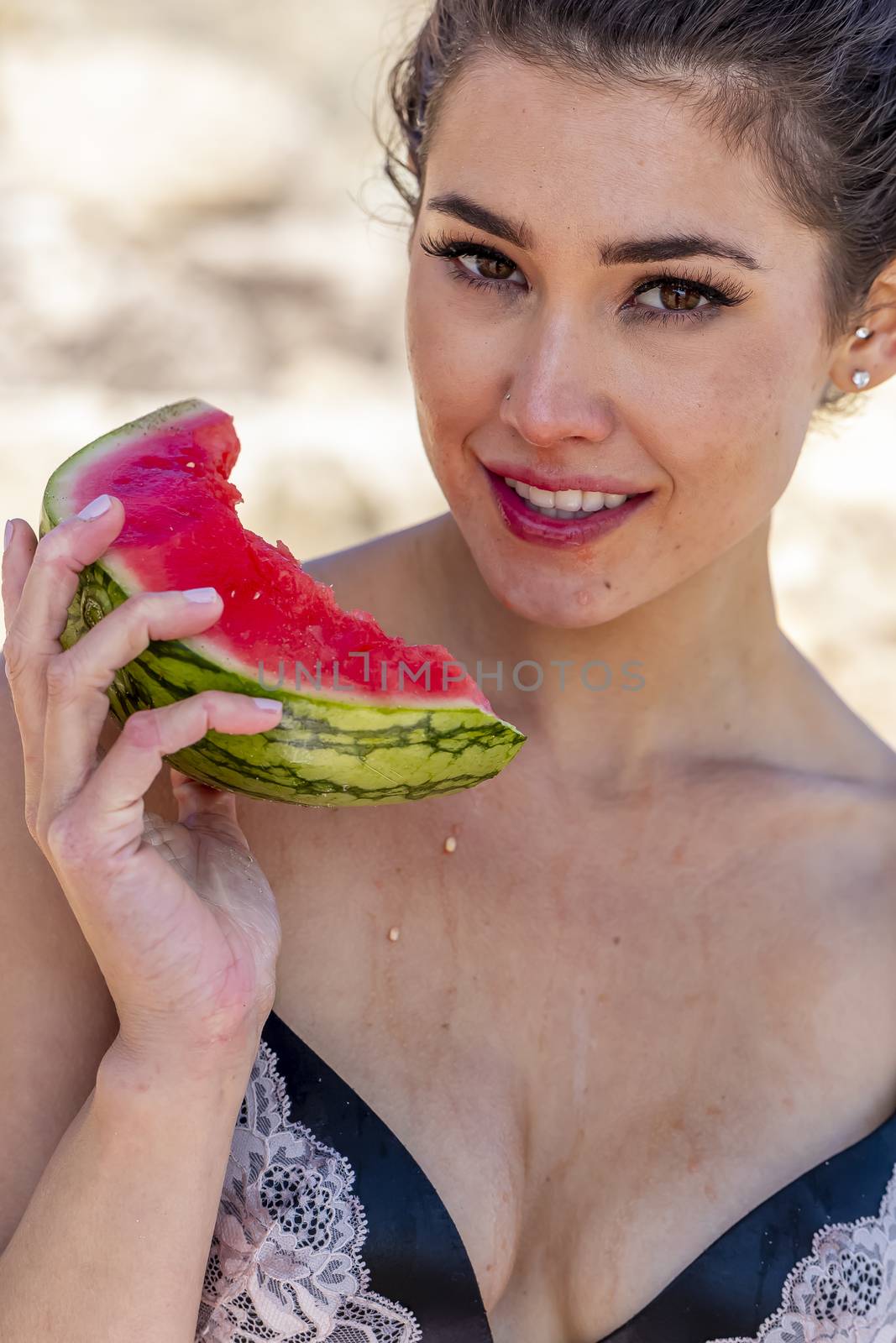 A gorgeous brunette bikini model enjoying watermelon at the beach on a sunny day