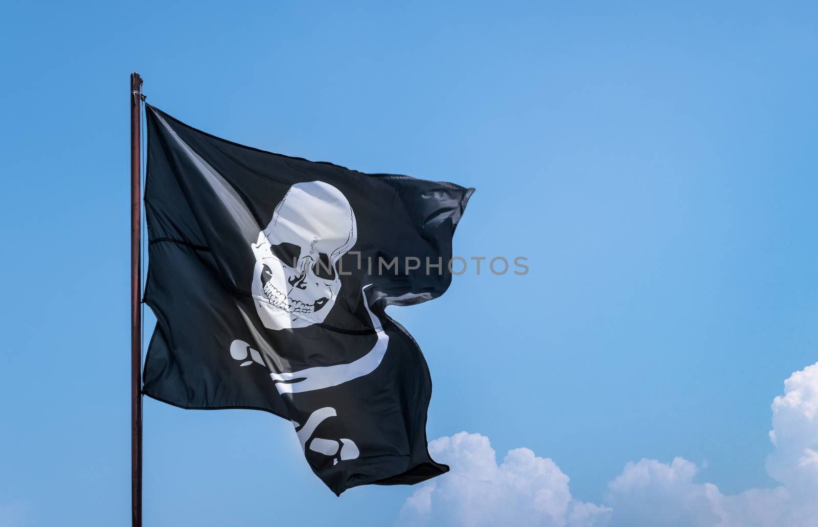 A flag evolving in the wind, depicting the skull and crossbones as a symbol of pirates. Pirate flag against blue sky. Space for text