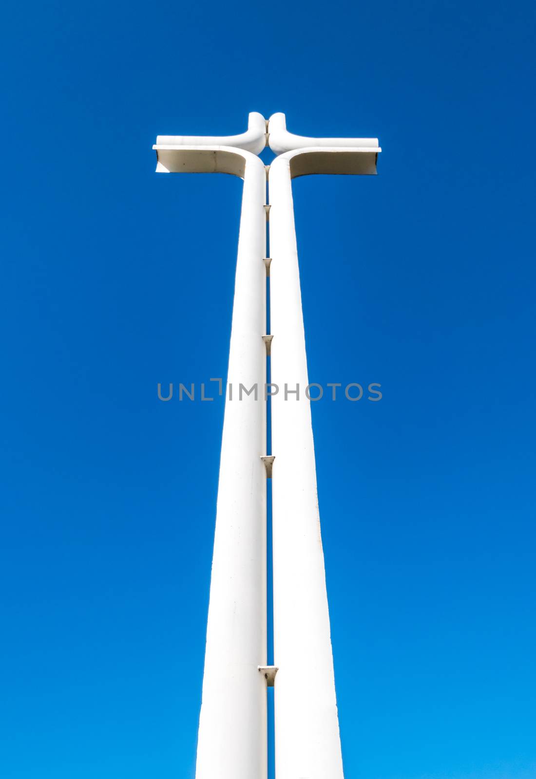 Modern iron cross of white color, isolated on a blue sky background.