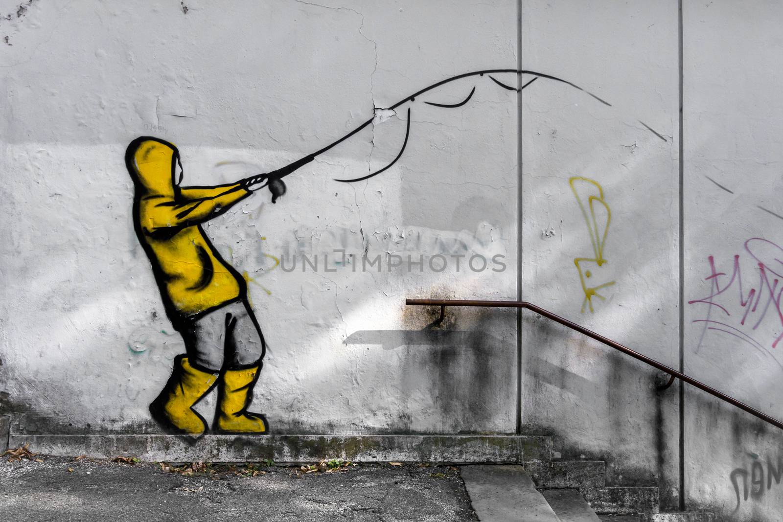 Street art by unknown artist on a concrete wall. The painting represents a boy fishing, suit with raincoat and yellow galoshes.