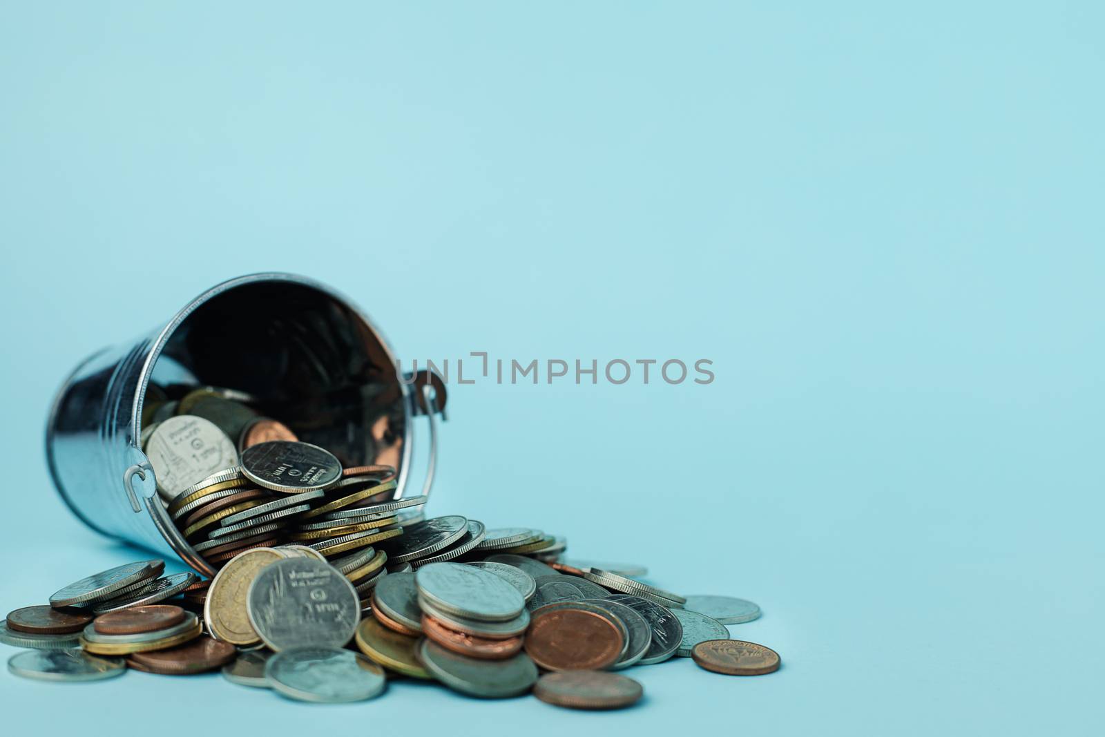 Pile of money coins with a tin bucket on blue background for investment, business, finance and saving money concept 
