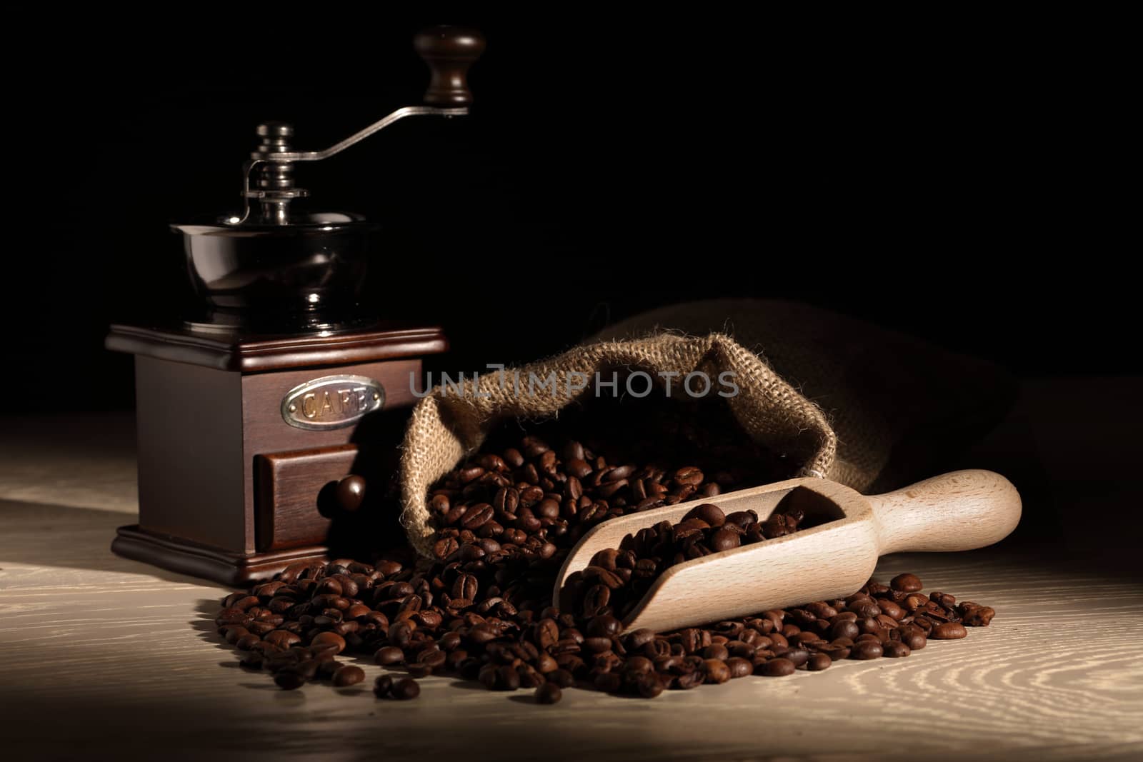 Coffee beans with a scoop grinder and hessian sack on wooden surface