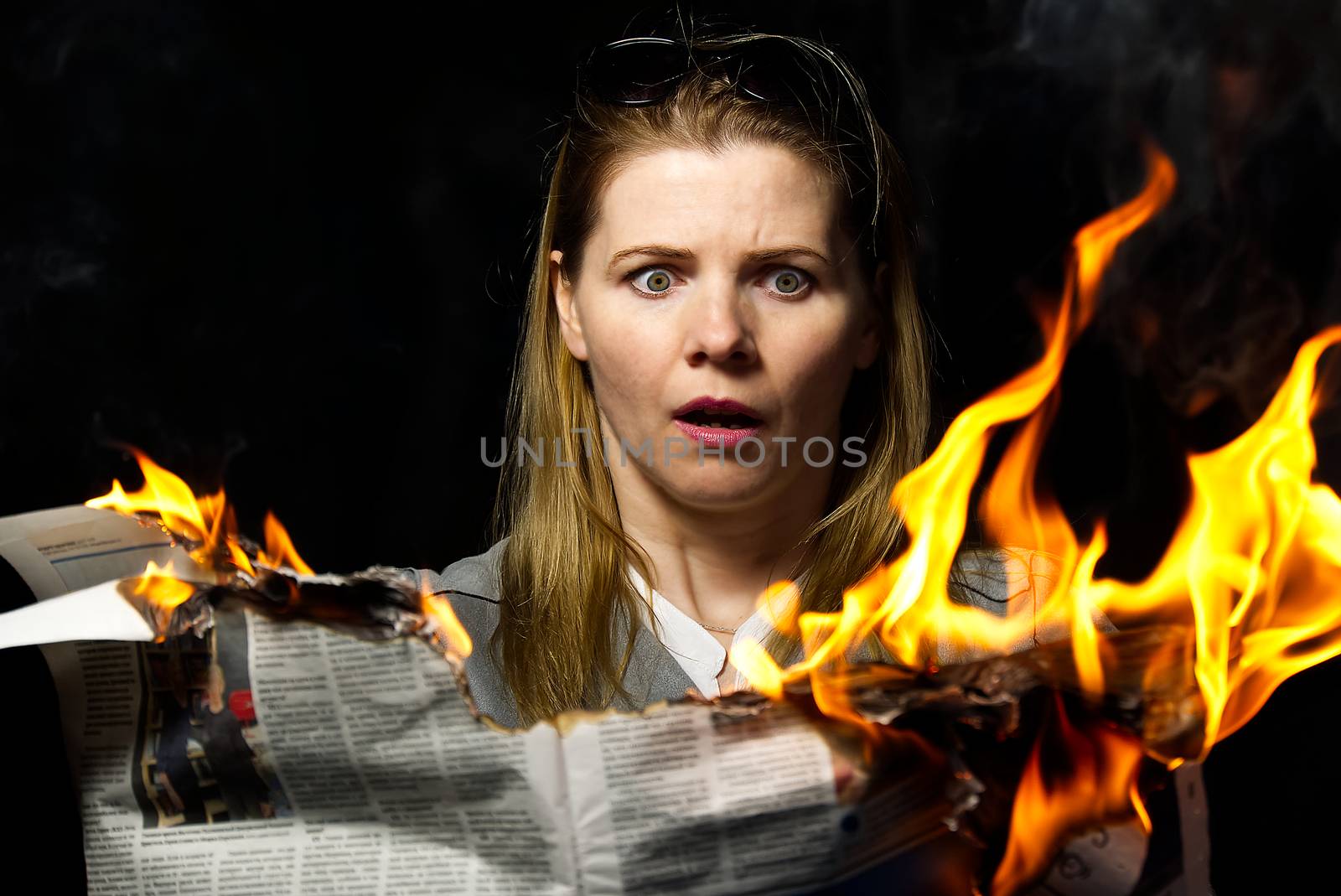 A woman is holding a burning newspaper. Fake news concept. by PhotoTime