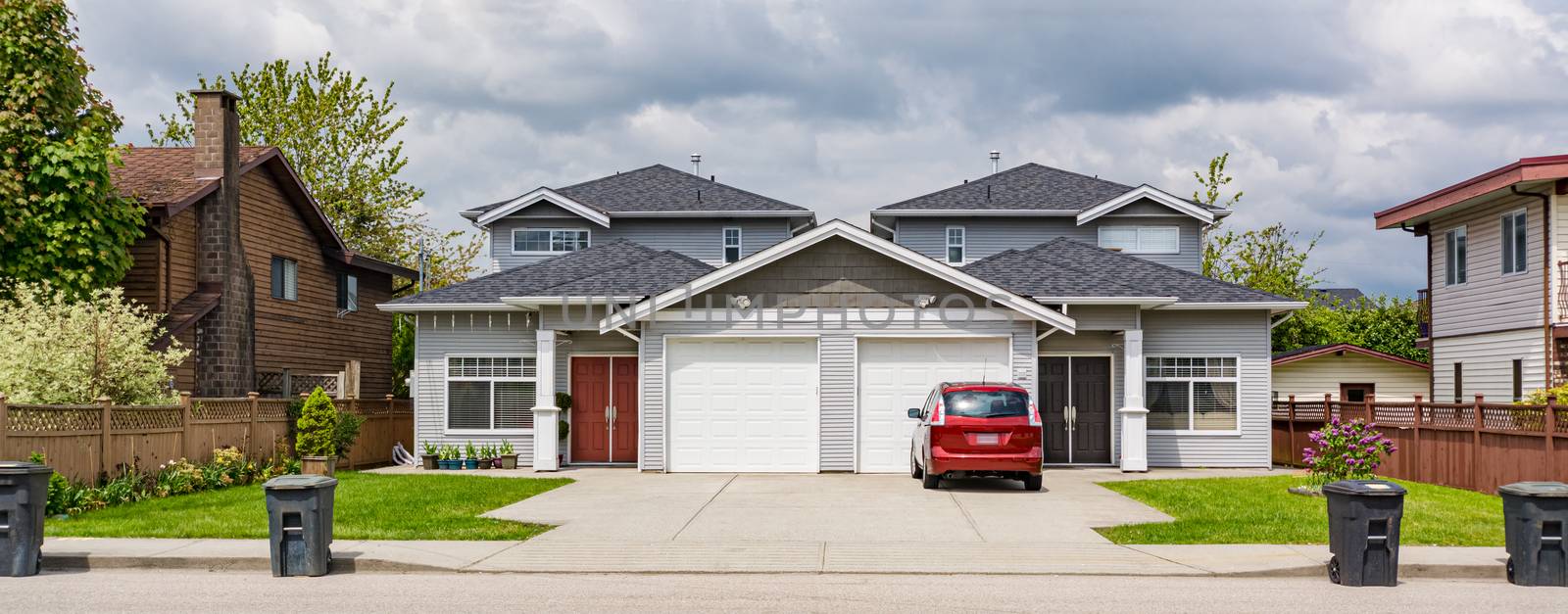 Residential duplex townhouse with red car parked on concret driveway and garbage bins on the road in front