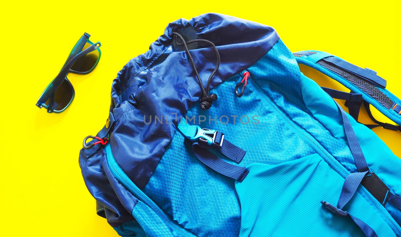 Large blue backpack and sun glasses. to travel trip isolated on yellow background.