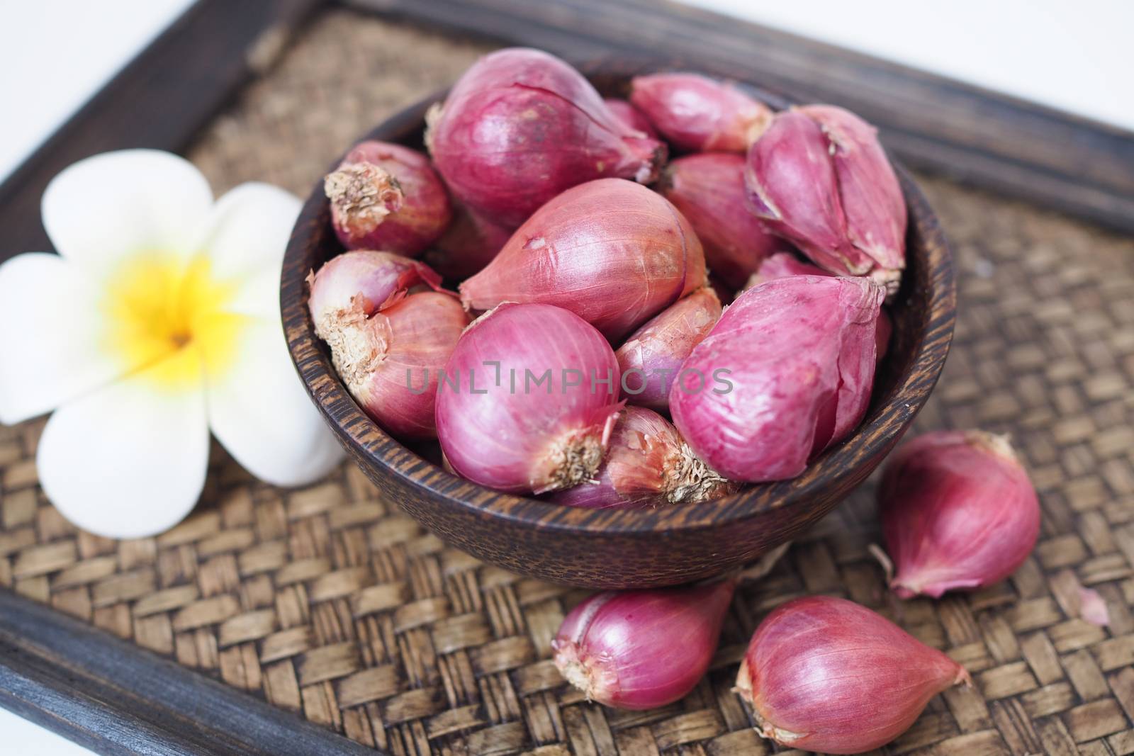 Red shallots in a bowl, placed on an old wooden tray bamboo weave.