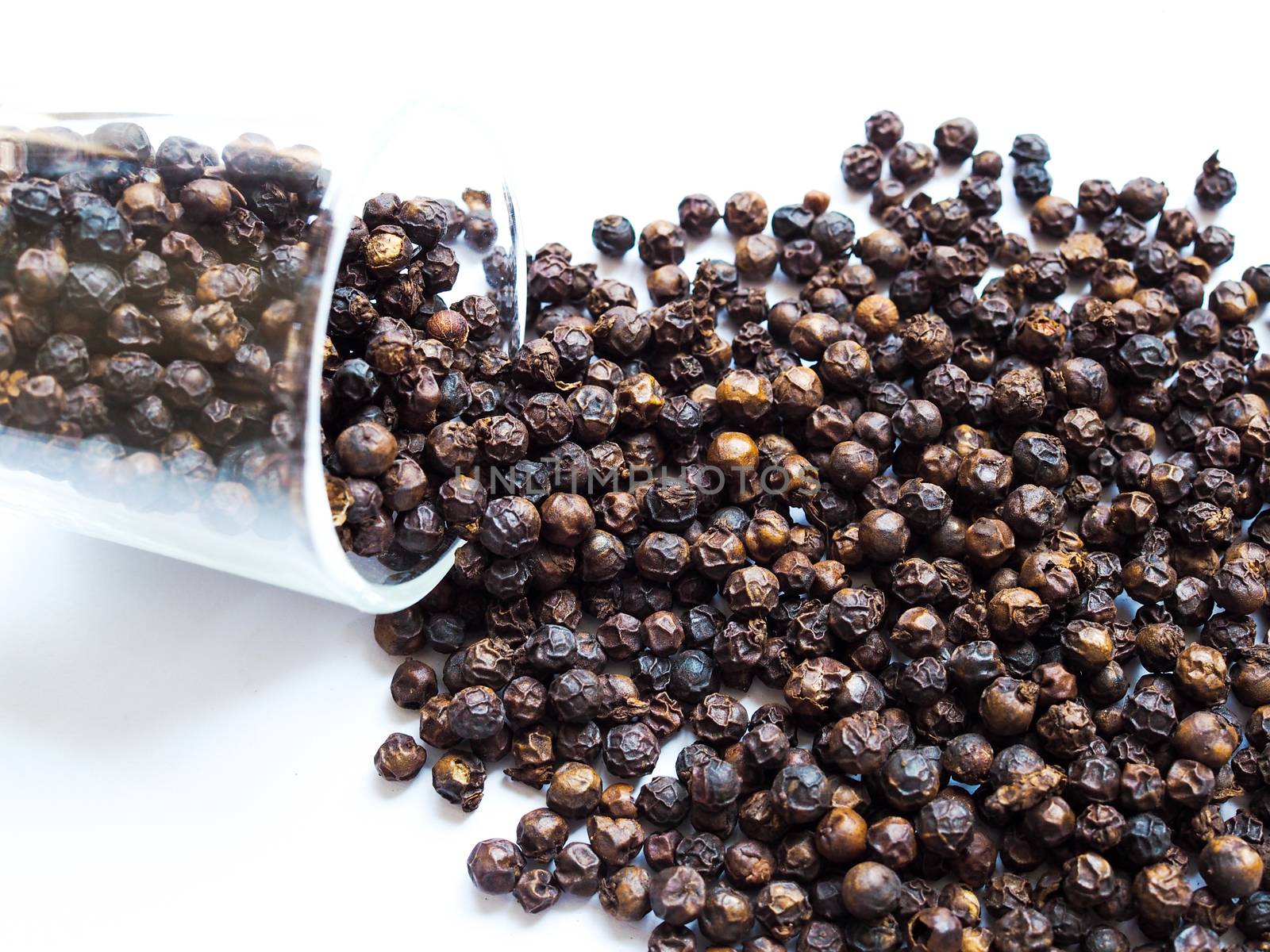 Dried black pepper seeds, peppercorn in a clear glass isolated on white background