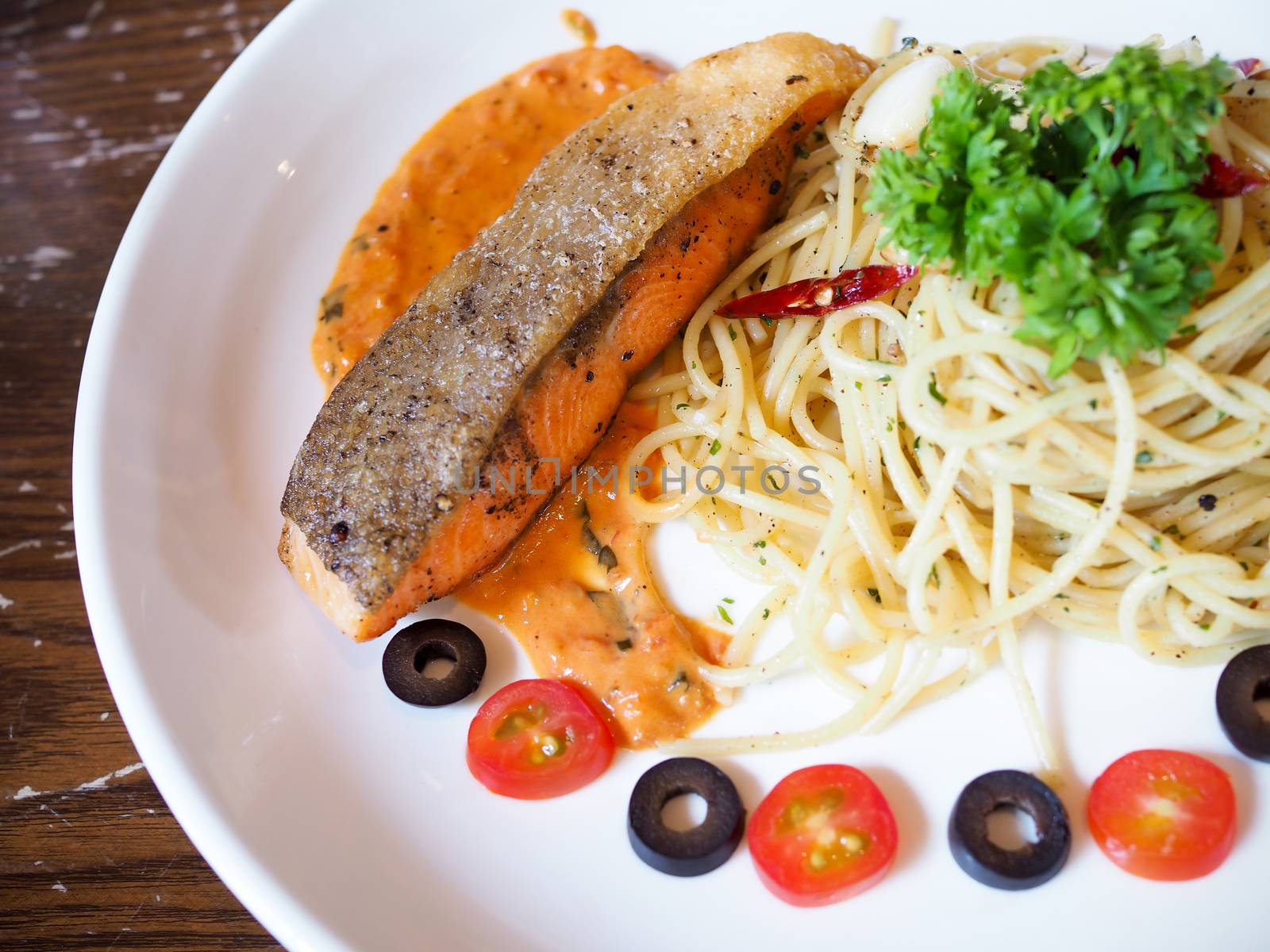 Food with spaghetti and salmon steak in white ceramic plate on table.