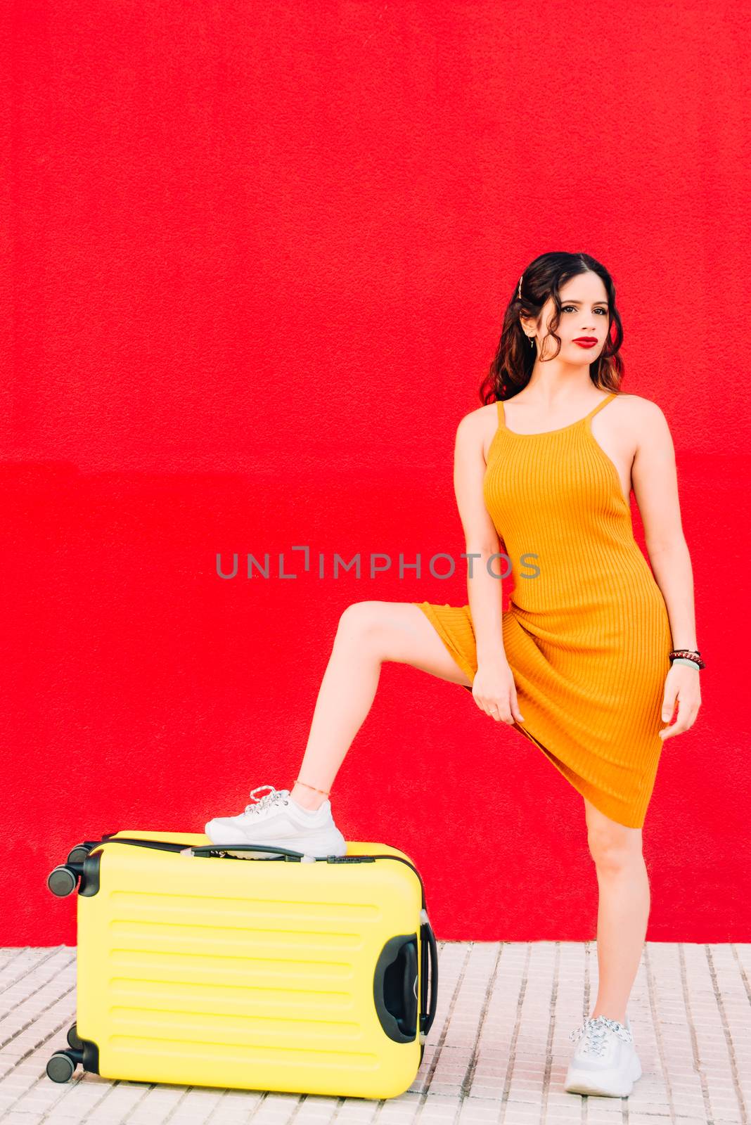 young woman stepping on a yellow suitcase.