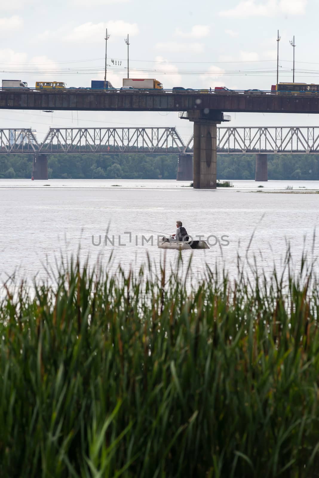 A fisherman on a boat on the Dnieper River in Kiev, Ukraine, close to the Pivnichnyi bridge (ex Moskovsky)