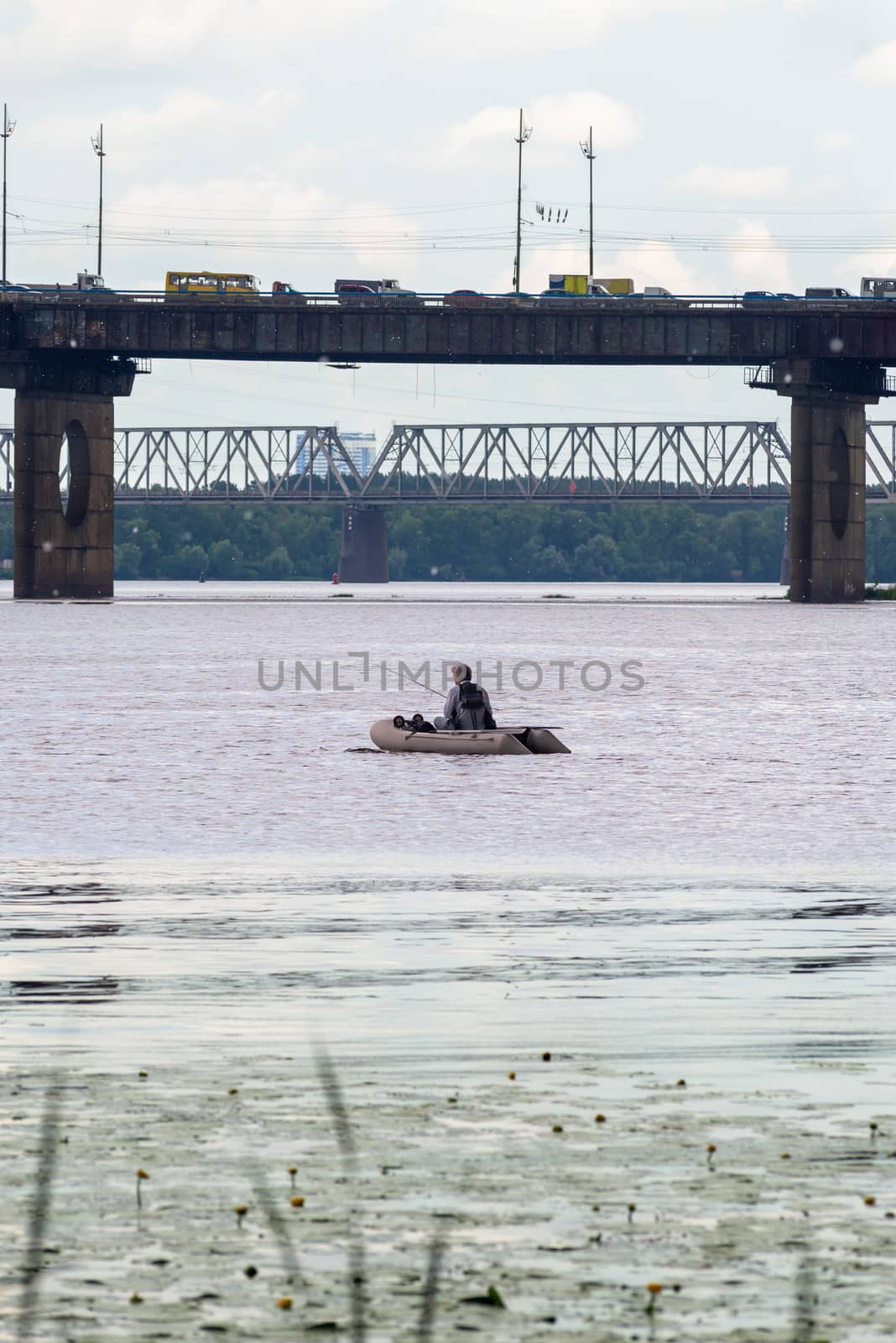 A fisherman on a boat on the Dnieper River in Kiev, Ukraine, close to the Pivnichnyi bridge (ex Moskovsky)