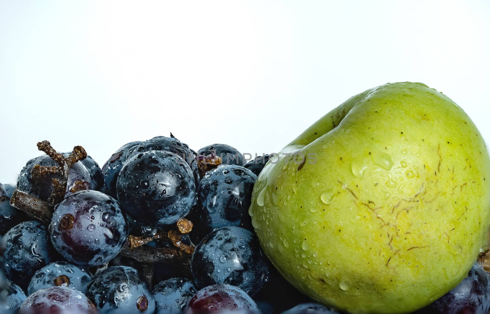 Bright purple grapes and green apples in a wooden basket on a white background.