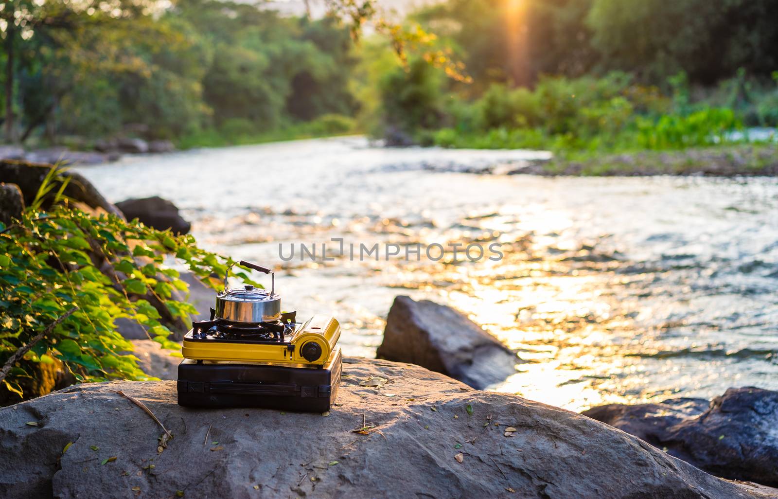 Picnic gas stove and aluminum teapot for boiling water during camping near the river