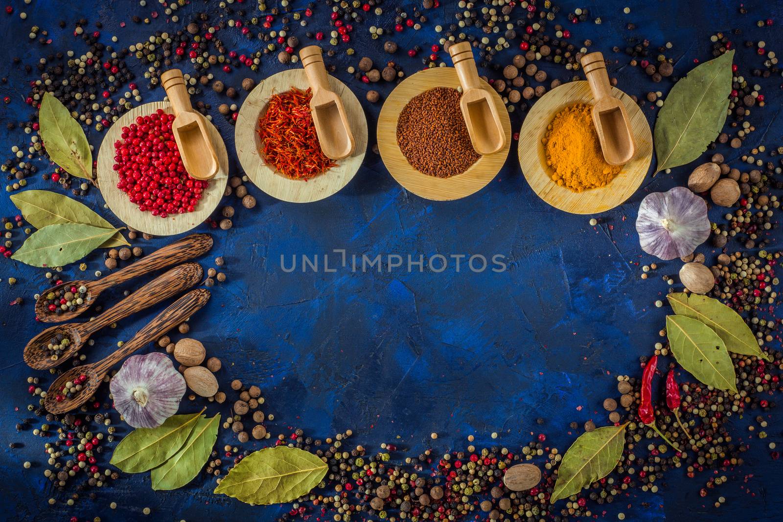 Assortment of colorful spices in the wooden bowls with spoons on a dark blue background. Curry, saffron, pink peppercorns, star anise, pepper, hot chili, garlic, bay leaf, nutmeg. Top view. Copy space.