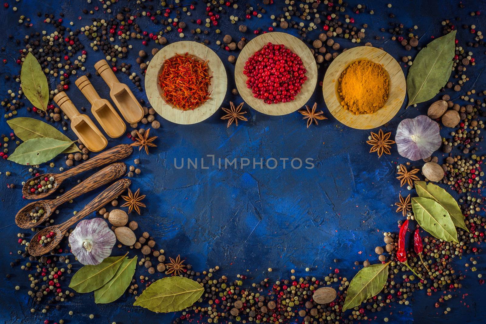 Assorted spices in the wooden bowls with spoons on a dark blue background. Spices concept- Cooking at home. Curry, saffron, pink peppercorns, star anise, hot chili, garlic, bay leaf, nutmeg. Top view.  Copy space.