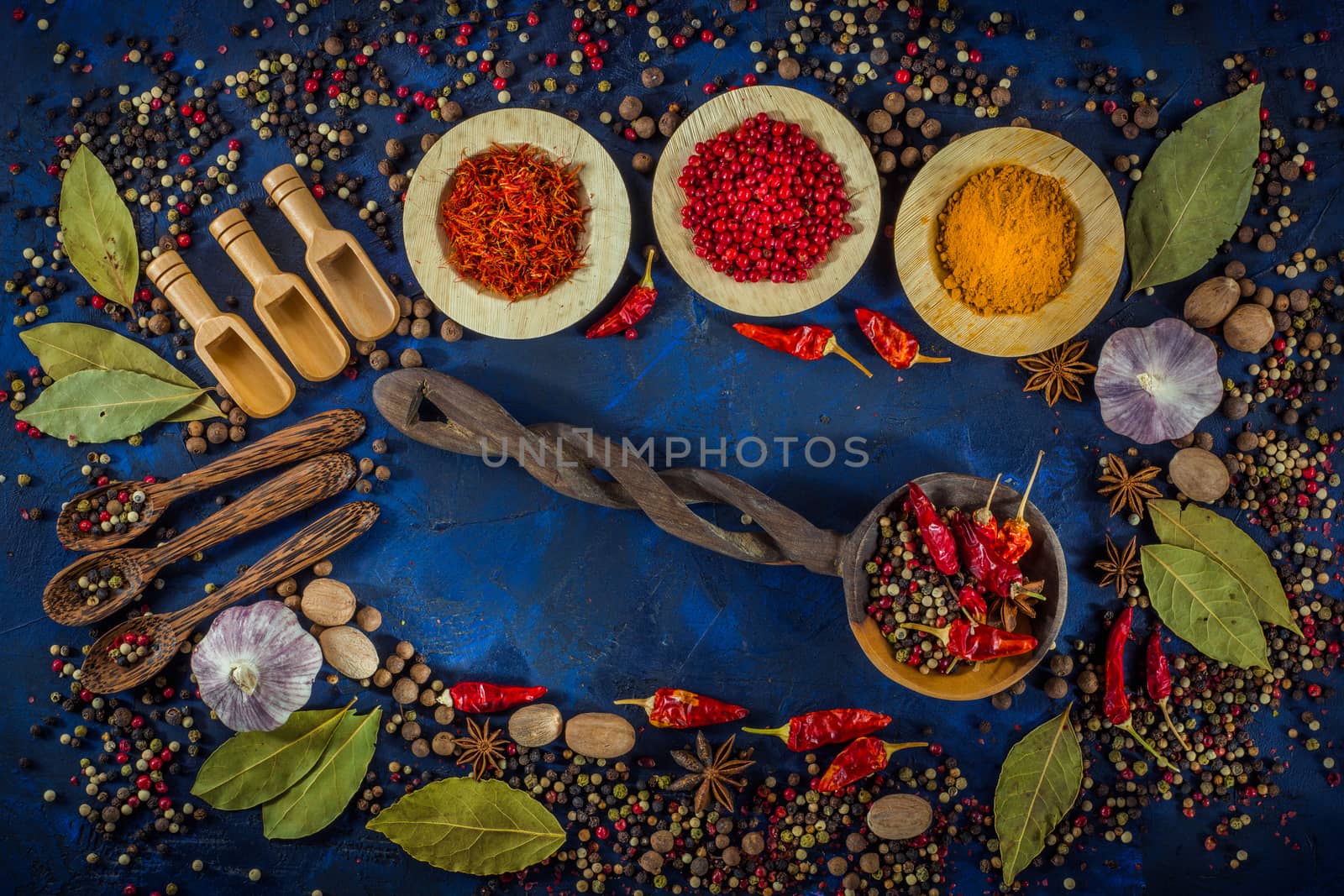 Various fragrant spices and herbs on a dark blue background. Spicy background with pepper mix and other spices. Colorful spices for cooking with vintage handmade wooden spoon. Top view, flat-lay.