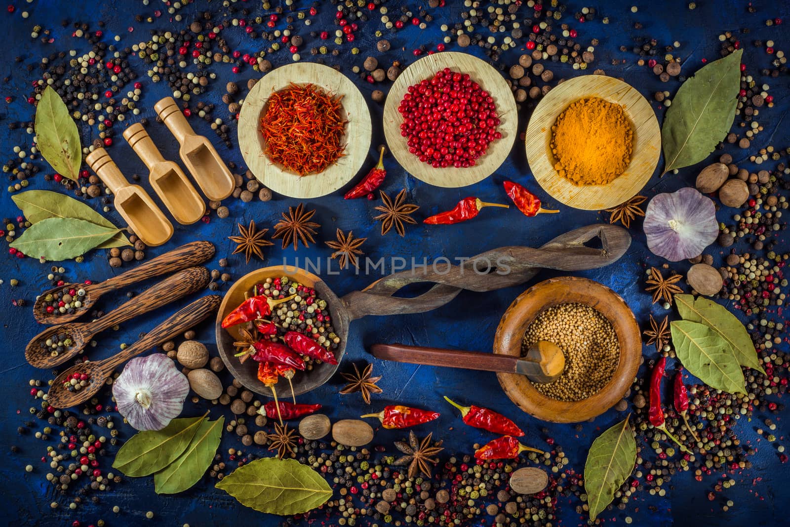 Various fragrant spices and herbs on a dark blue background. Spicy background with pepper mix and other spices. Colorful spices for cooking with vintage handmade wooden spoon and bowl. Top view, flat-lay.