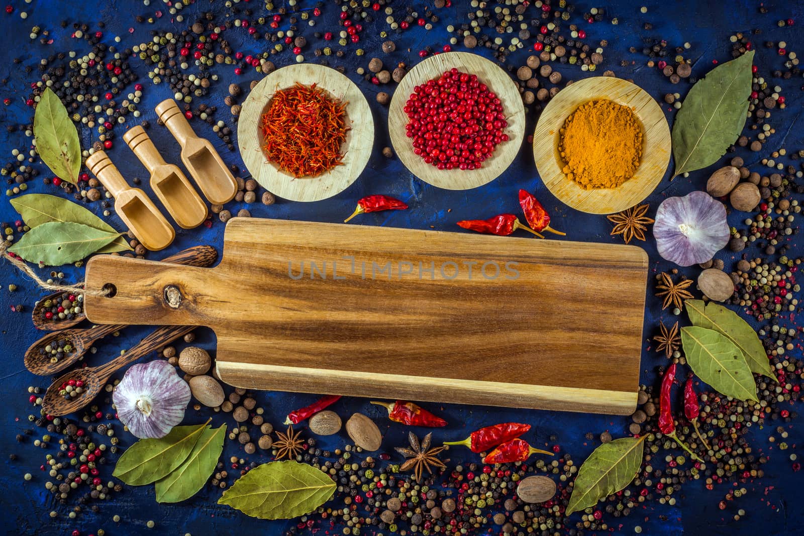 Various spices and wooden spoons on a dark blue background. Spicy background with pepper mix with wooden cutting board.  Spices concept- Cooking at home. Top view, close up, flat-lay.