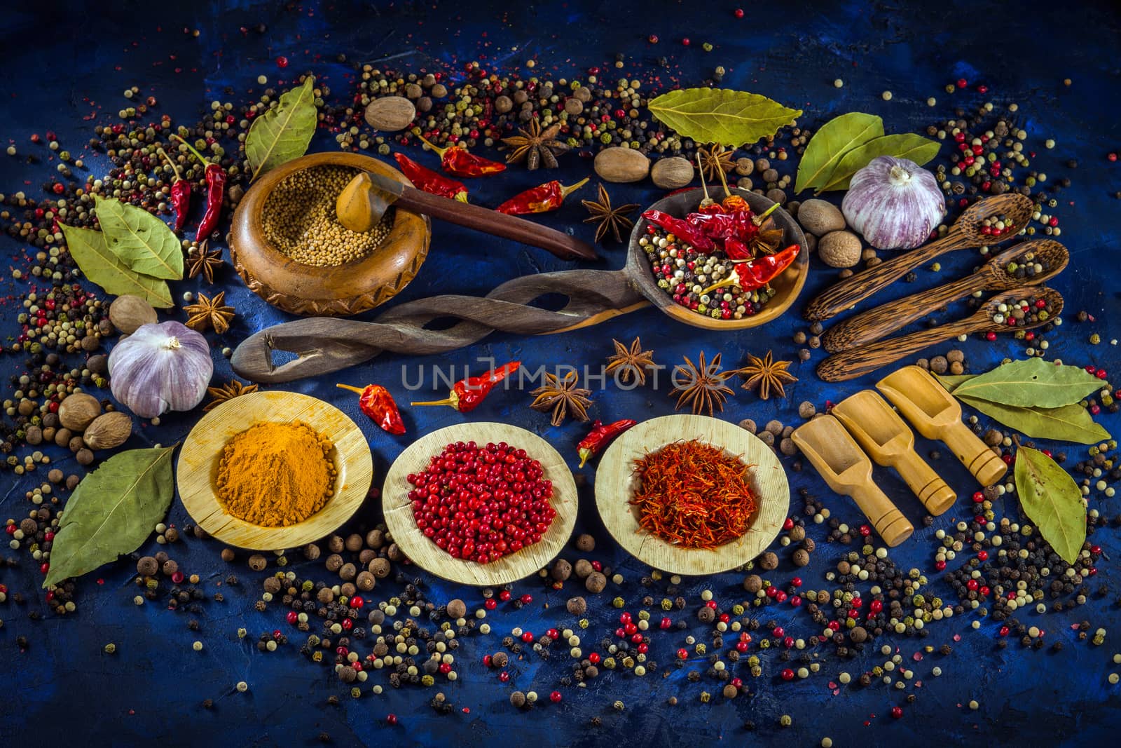 Various fragrant spices and herbs on a dark blue background. Spicy background with pepper mix and other spices. Colorful spices for cooking with vintage handmade wooden spoon and bowl. Top view, flat-lay.