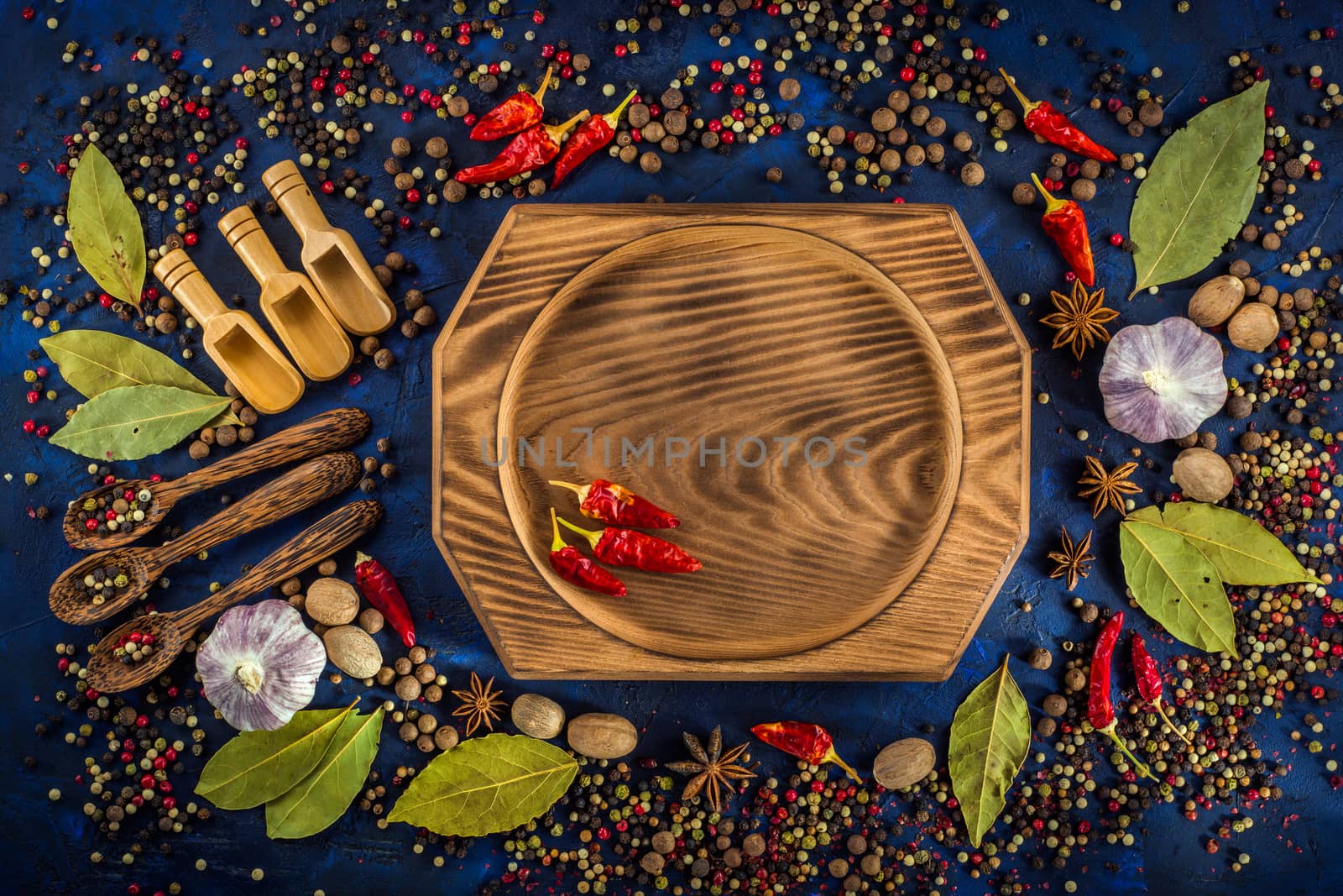 Assortment of colorful spices on a dark blue background. Spicy background with pepper mix on a ceramic plate. Colorful spices for cooking with handmade wooden bowl. Top view, flat-lay.