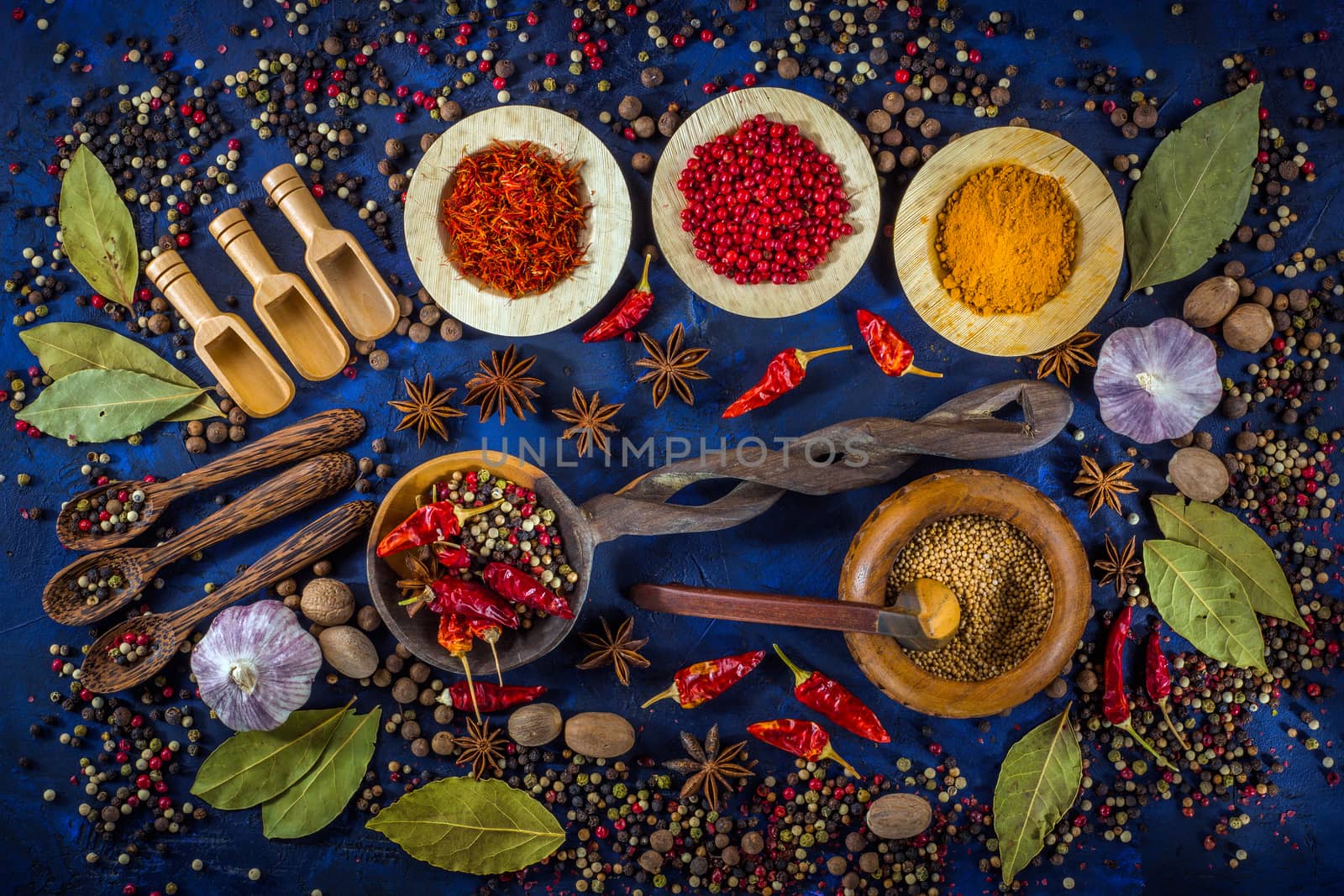 Various fragrant spices and herbs on a dark blue background. Spicy background with pepper mix and other spices. Colorful spices for cooking with vintage handmade wooden spoon and bowl. Top view, flat-lay.