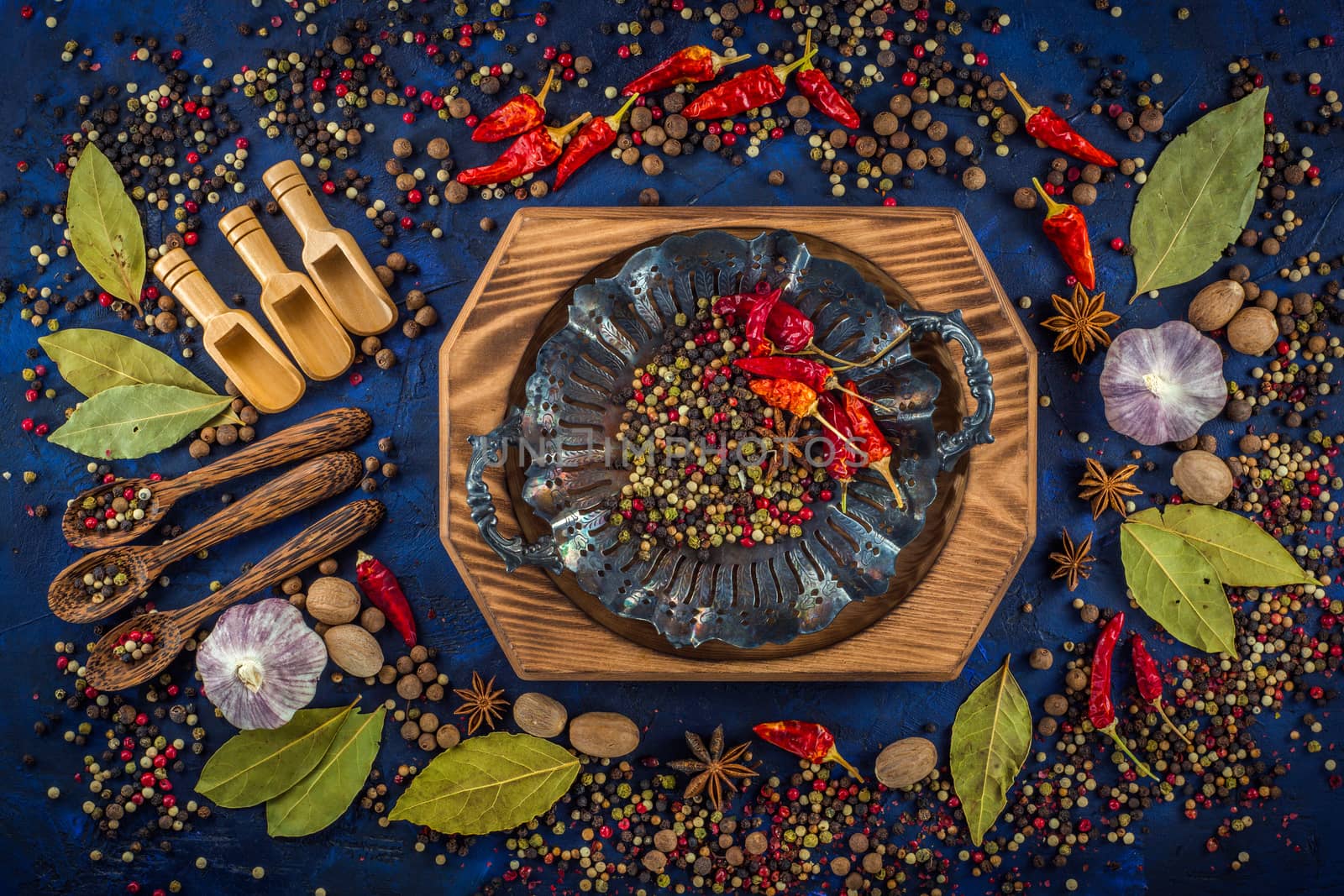 Assortment of colorful spices on a dark blue background. Spicy background with pepper mix on a vintage silver plate. Various spices, star anise, pepper, hot chili, garlic, bay leaf, nutmeg. Top view, flat-lay.