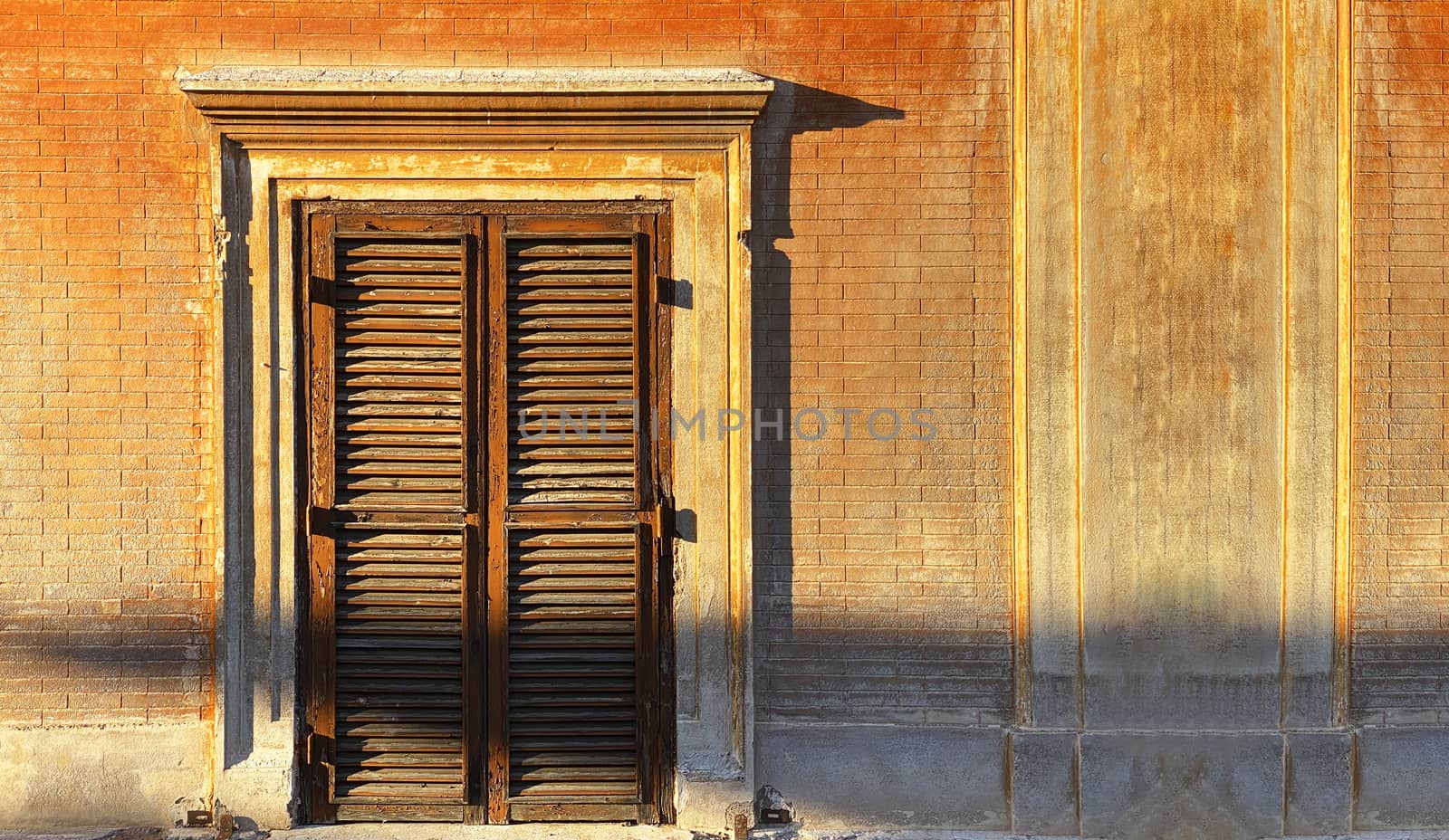 Ancient window with closed wooden shutters illuminated by the sunlight at sunset in Italy. by rarrarorro