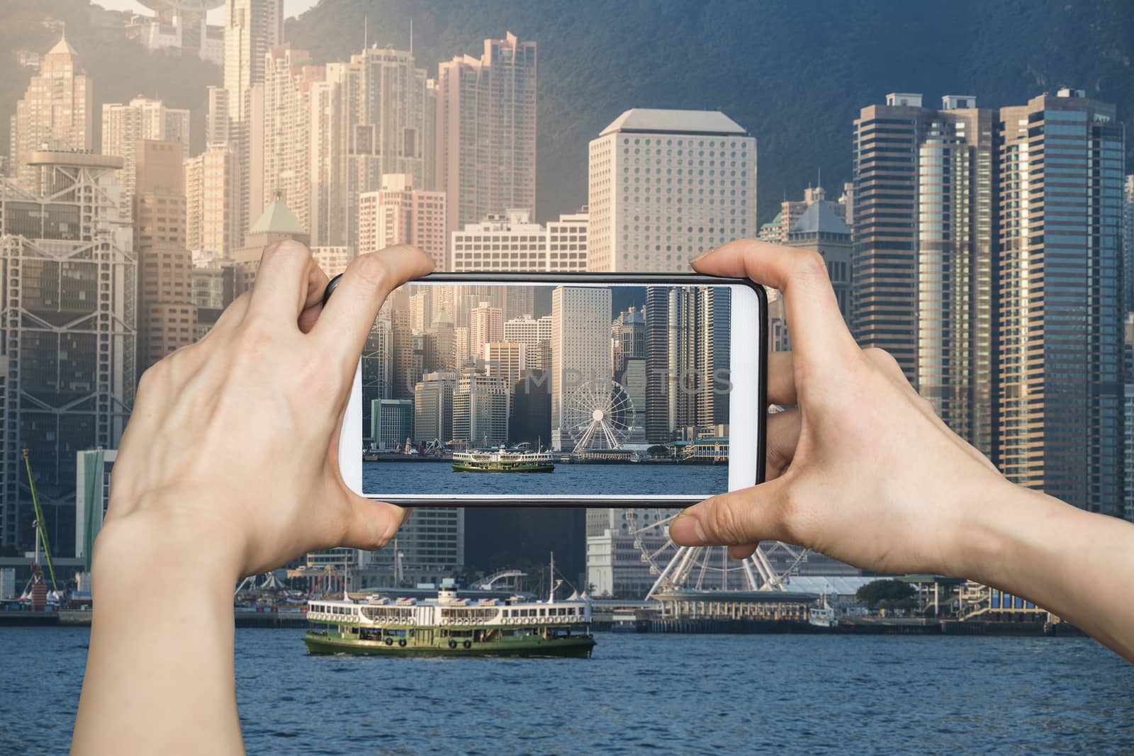 Girl taking pictures on mobile smart phone in Hong Kong's Victoria Harbour in sunrise