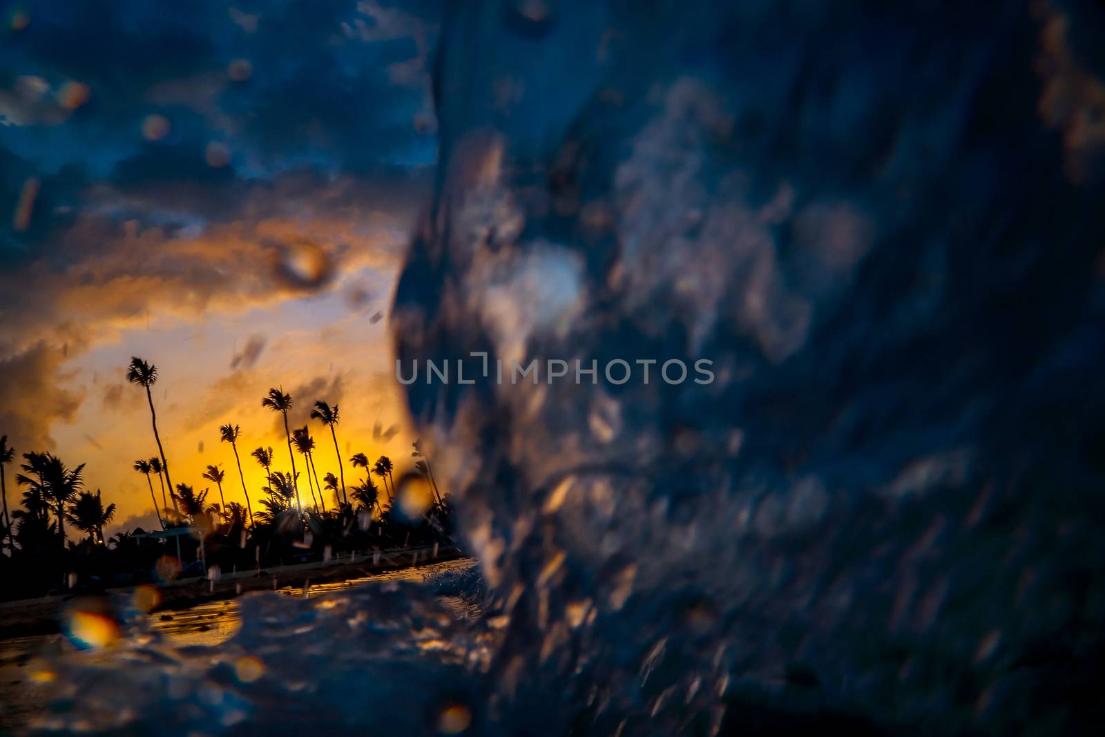 Sea wave close up, low angle view, sunset shot. Orange sunset on a tropical island in the ocean. Silhouettes of palm trees on the fion of a beautiful multi-colored sunset.