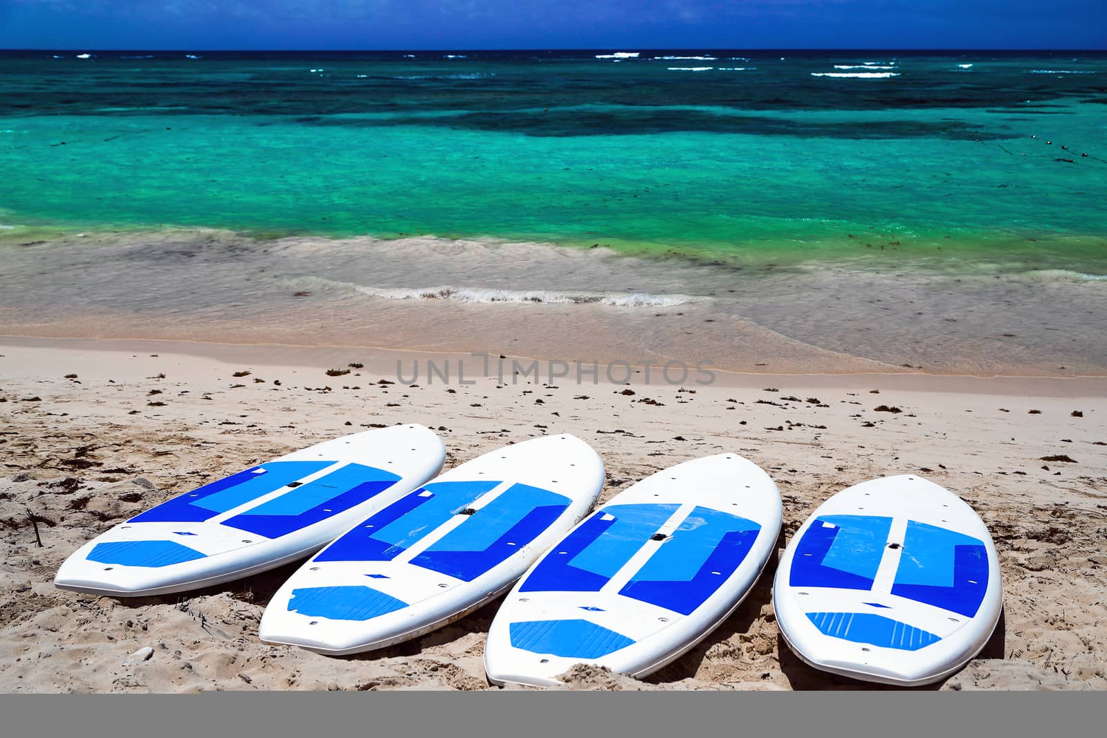 Surfboards on the beach. Surfing board on the beach with ocean view nobody. surfboards abandoned on an empty sandy beach with waves in distance. Summer sunny day on the shores of the Atlantic Ocean. Emerald water with white sand and blue sky. Bavaro beach.