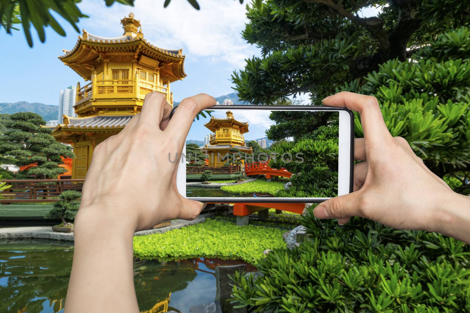 Girl taking pictures on mobile smart phone in Front View The Golden Pavilion Temple in Nan Lian Garden