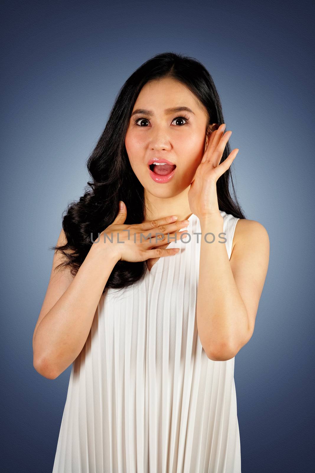 Shocked woman wearing white dress looking at camera and dark blue background with clipping path