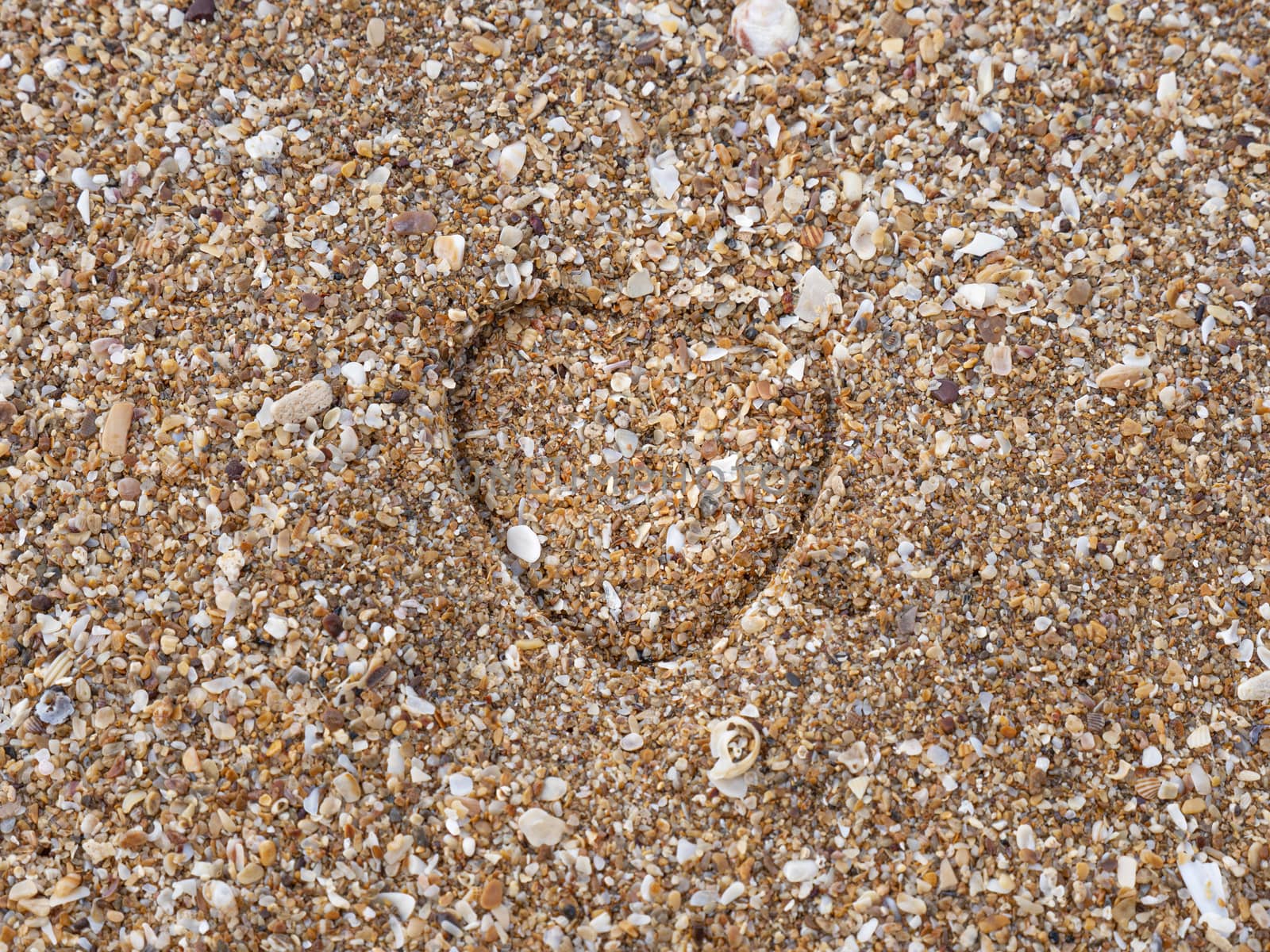 A heart impression on a sand at a sandy beach.