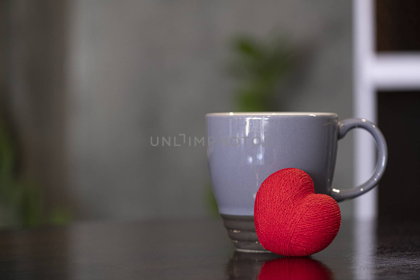 A grey ceramic coffee mug and a heart made of red string.