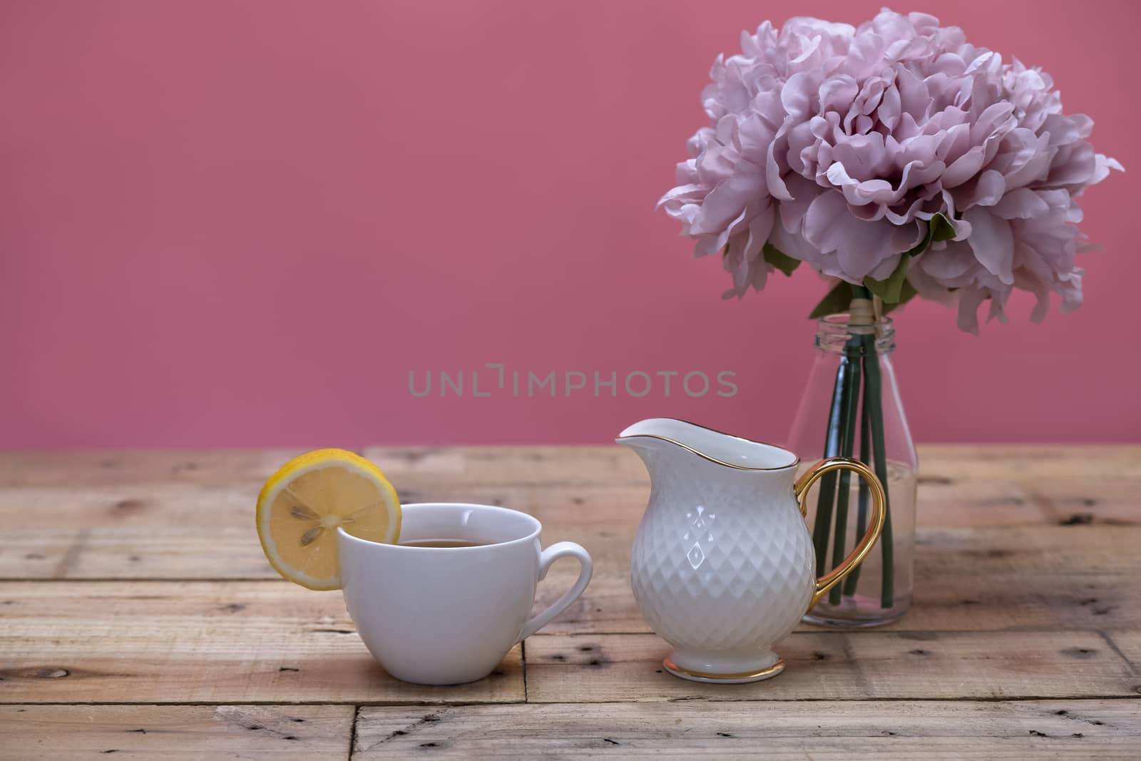 A serving of lemon tea with milk in white porcelain cup and white milk jug. Wooden table background.