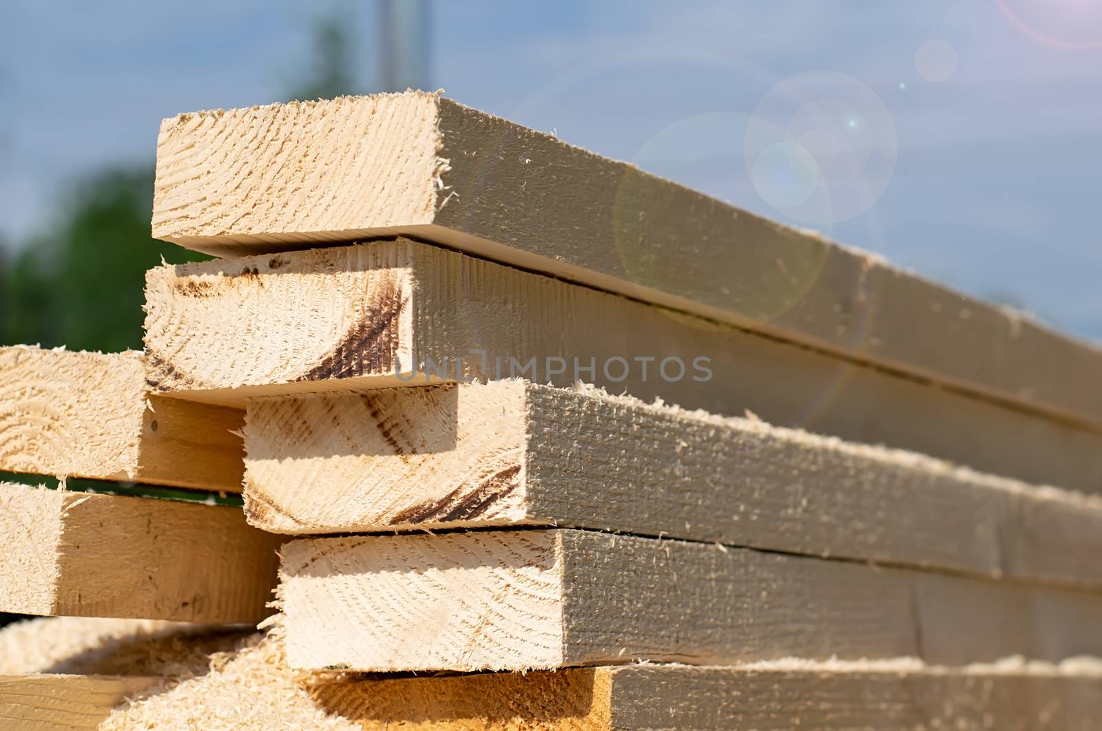 a pile of roughly sawn, cut long wooden bars, boards, lie in the open air on the street background the sky
