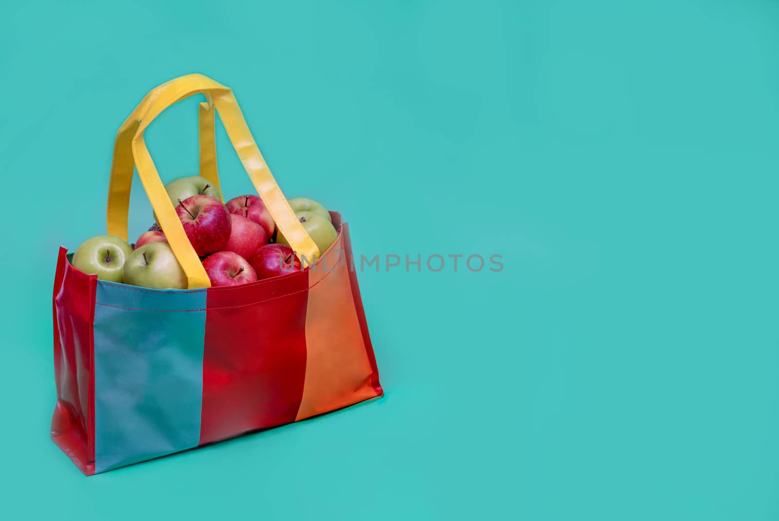 Red and green apples in colorful recycled plastic bag . Recycled plastic bag campaign advertising and healthy living concepts. Teal background.