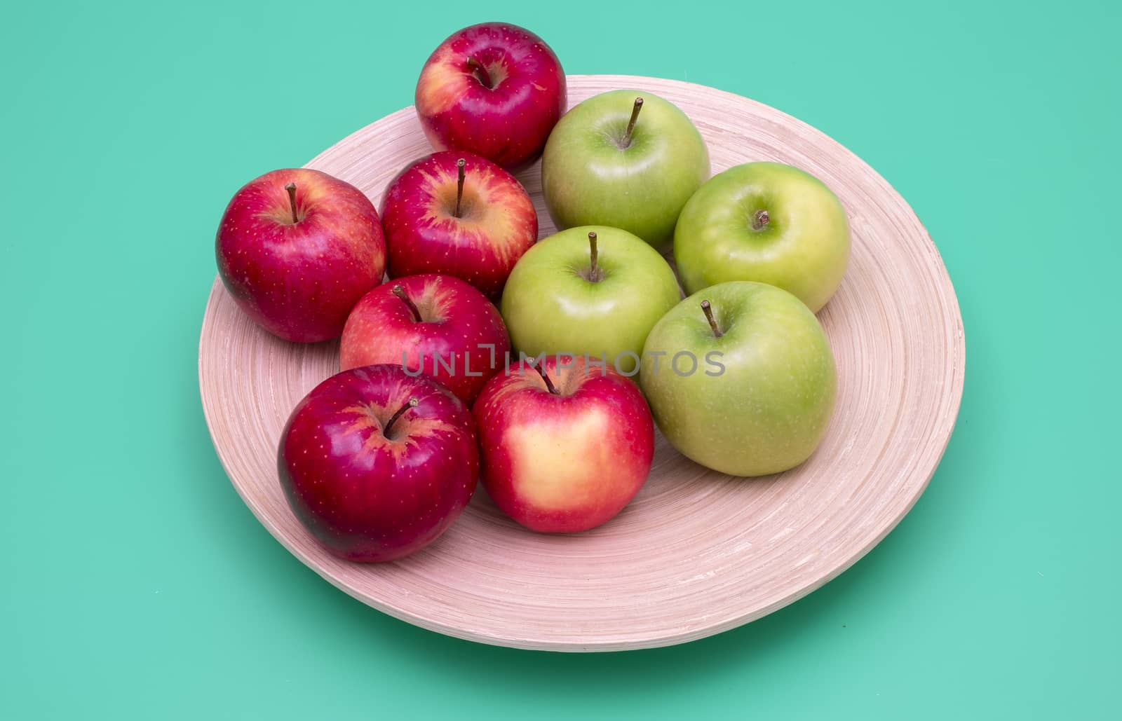 Red and green apples on a bamboo plate. Green background. Healthy eating concepts.